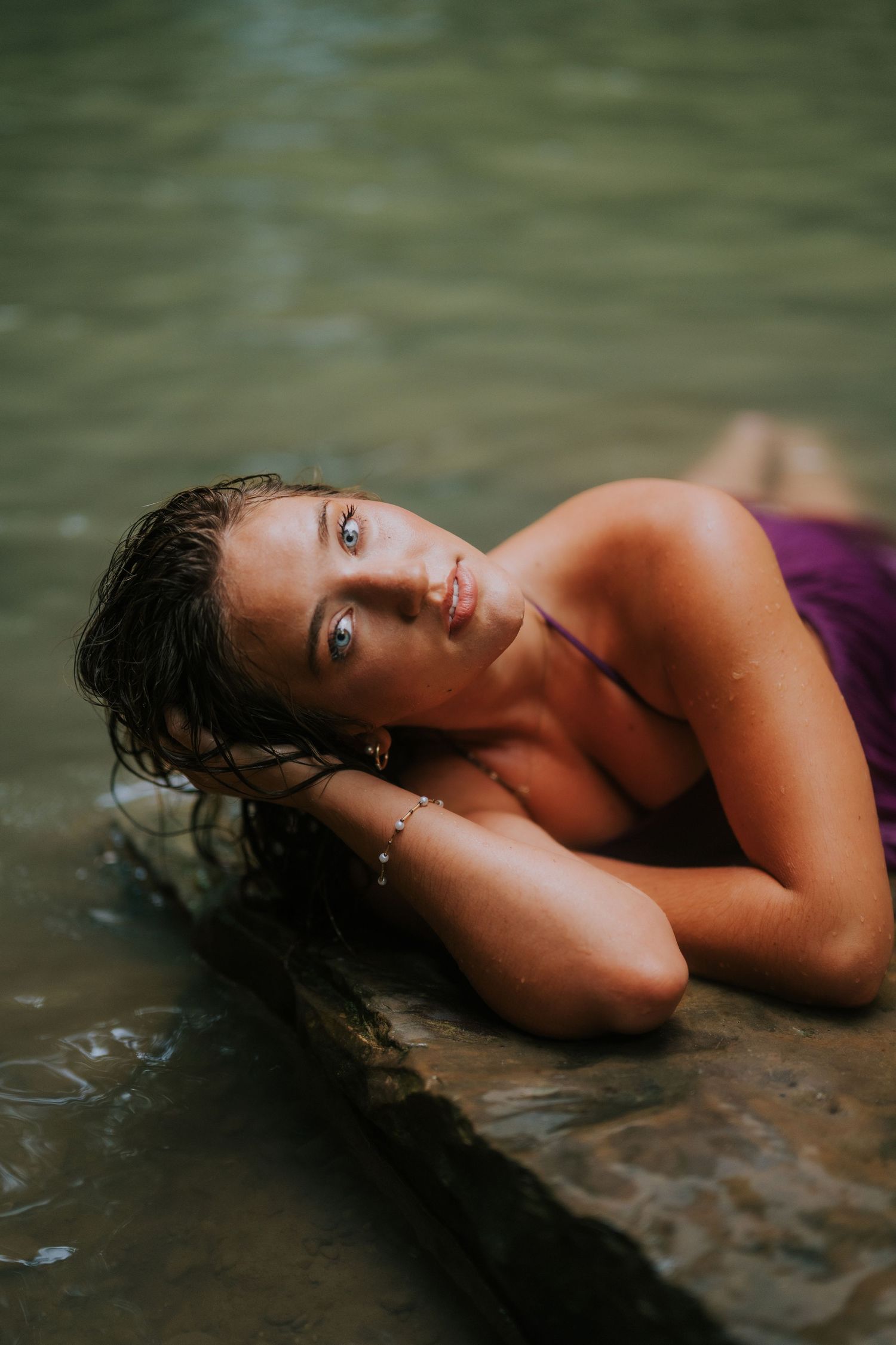 Person lying in shallow water during moody boudoir photoshoot.