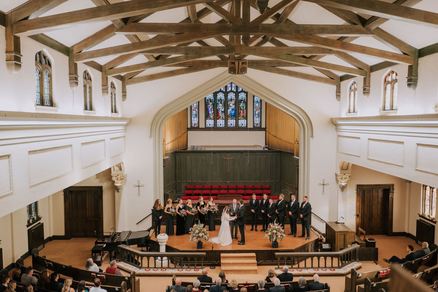 An elegant church ceremony takes place in a historic white chapel with exposed wooden beams and a pipe organ.