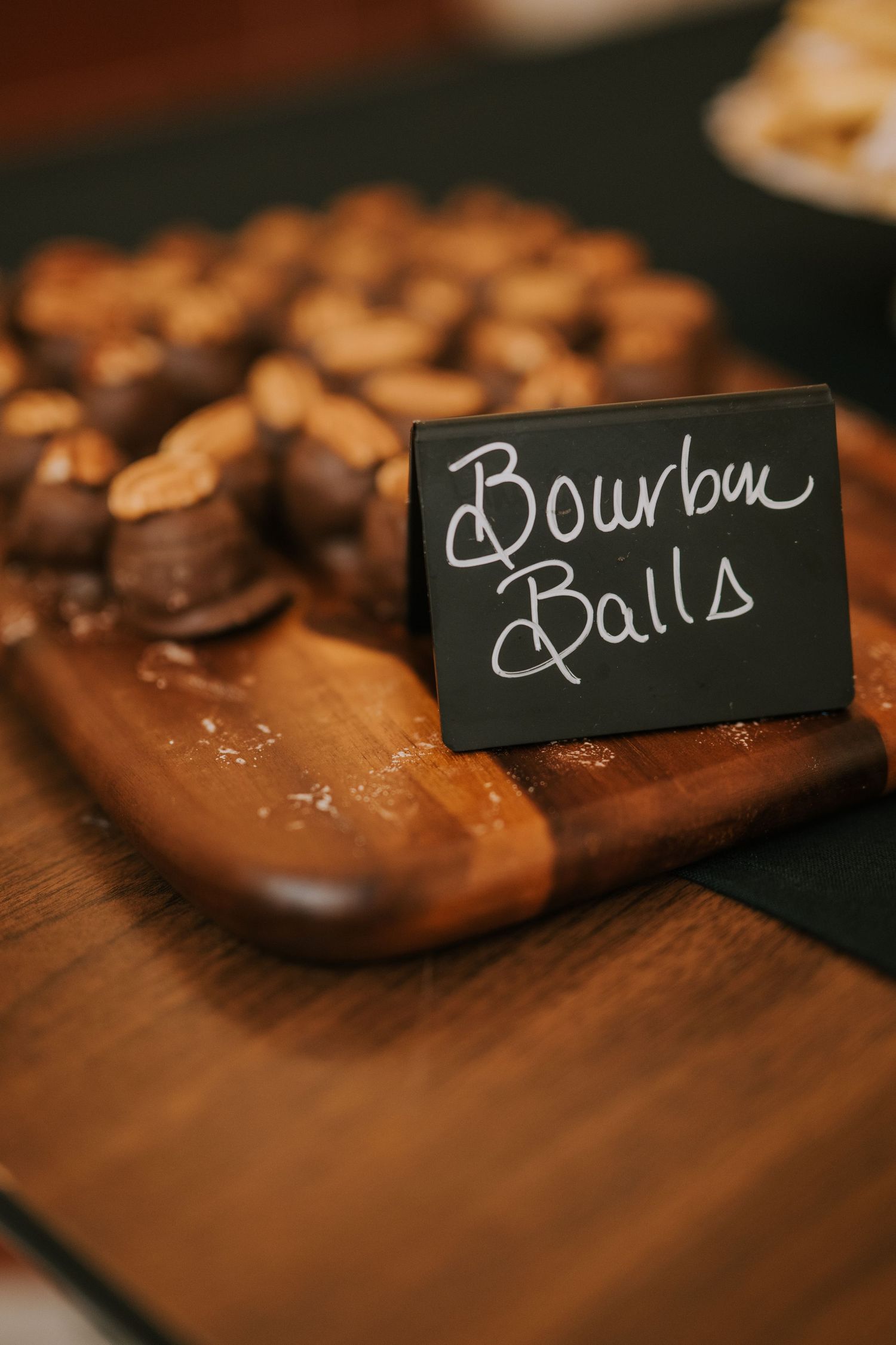 Bourbon balls displayed on a wooden cutting board with a small chalkboard sign at a dessert table.