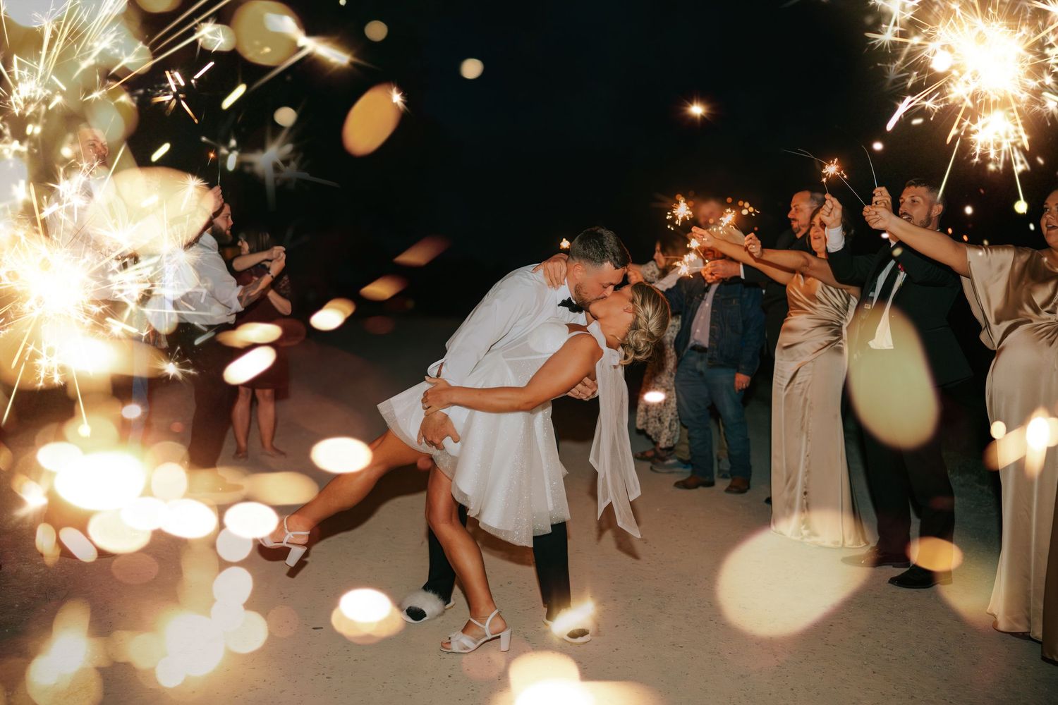 Wedding guests dance and celebrate on a dark dance floor illuminated by sparklers creating a magical atmosphere.
