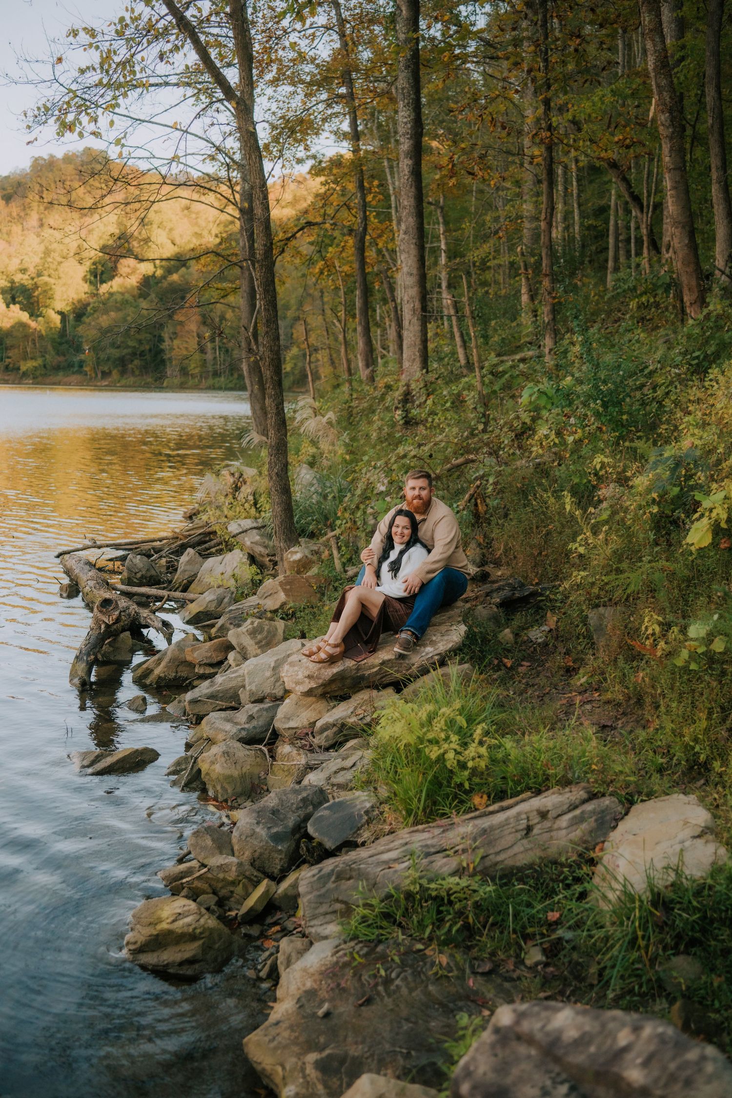 Family enjoying autumn afternoon on rocky shoreline by peaceful lake.