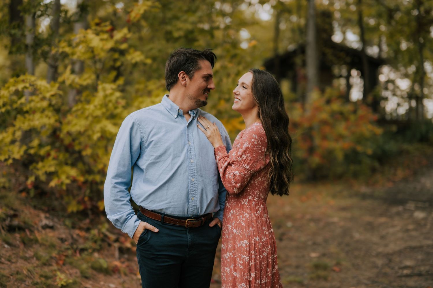 A couple shares a tender moment on an autumn forest trail with golden leaves in the background.