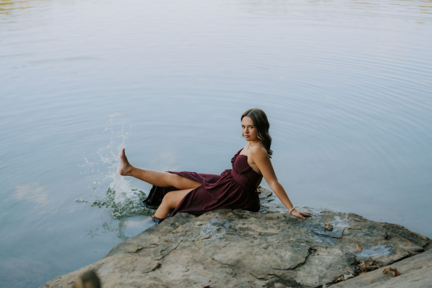 Person relaxing on rocky outcrop overlooking serene lake waters.