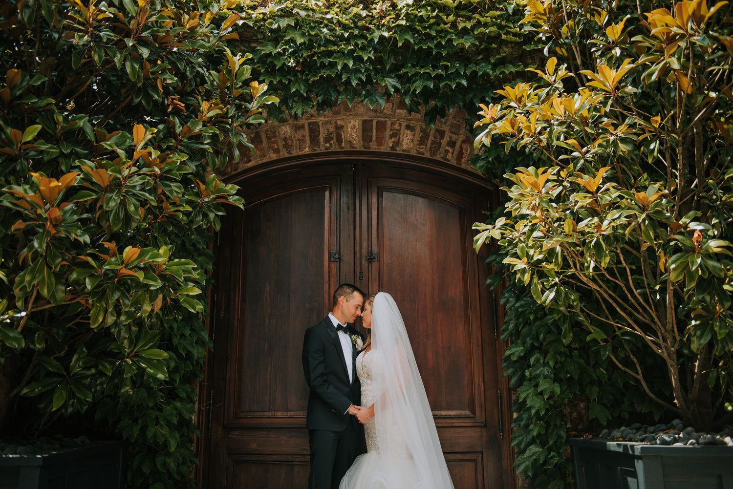 Romantic wedding portraits against wooden doors with lush greenery and florals.