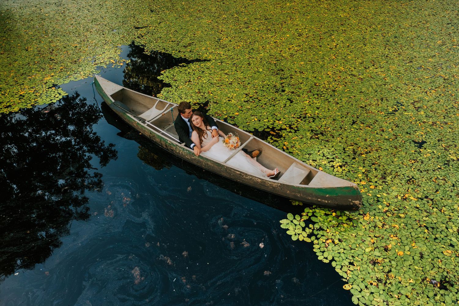 Row boat glides through tranquil water covered in green aquatic plants.