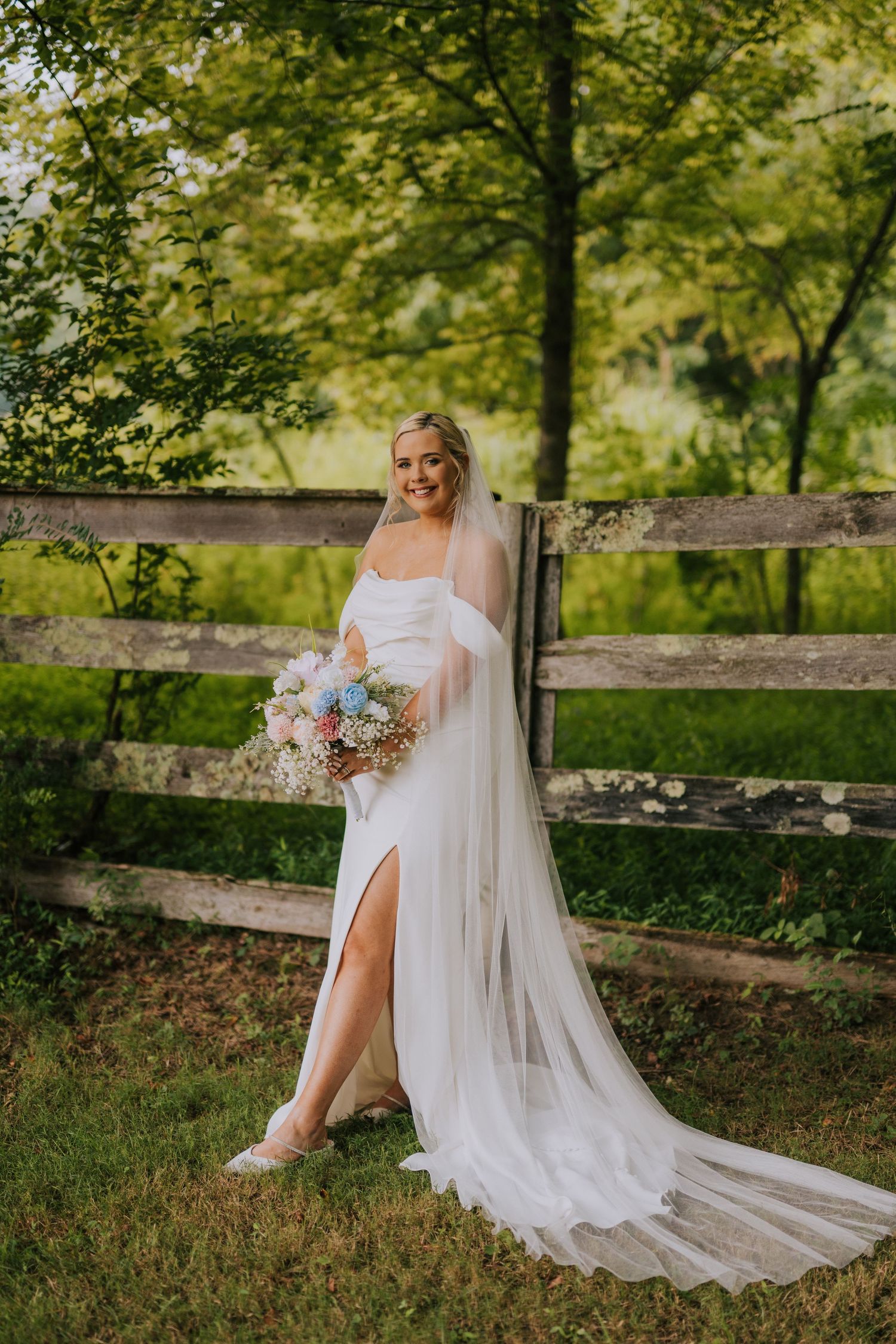 Ethereal bridal portrait with flowing veil and pastel bouquet in a garden setting.