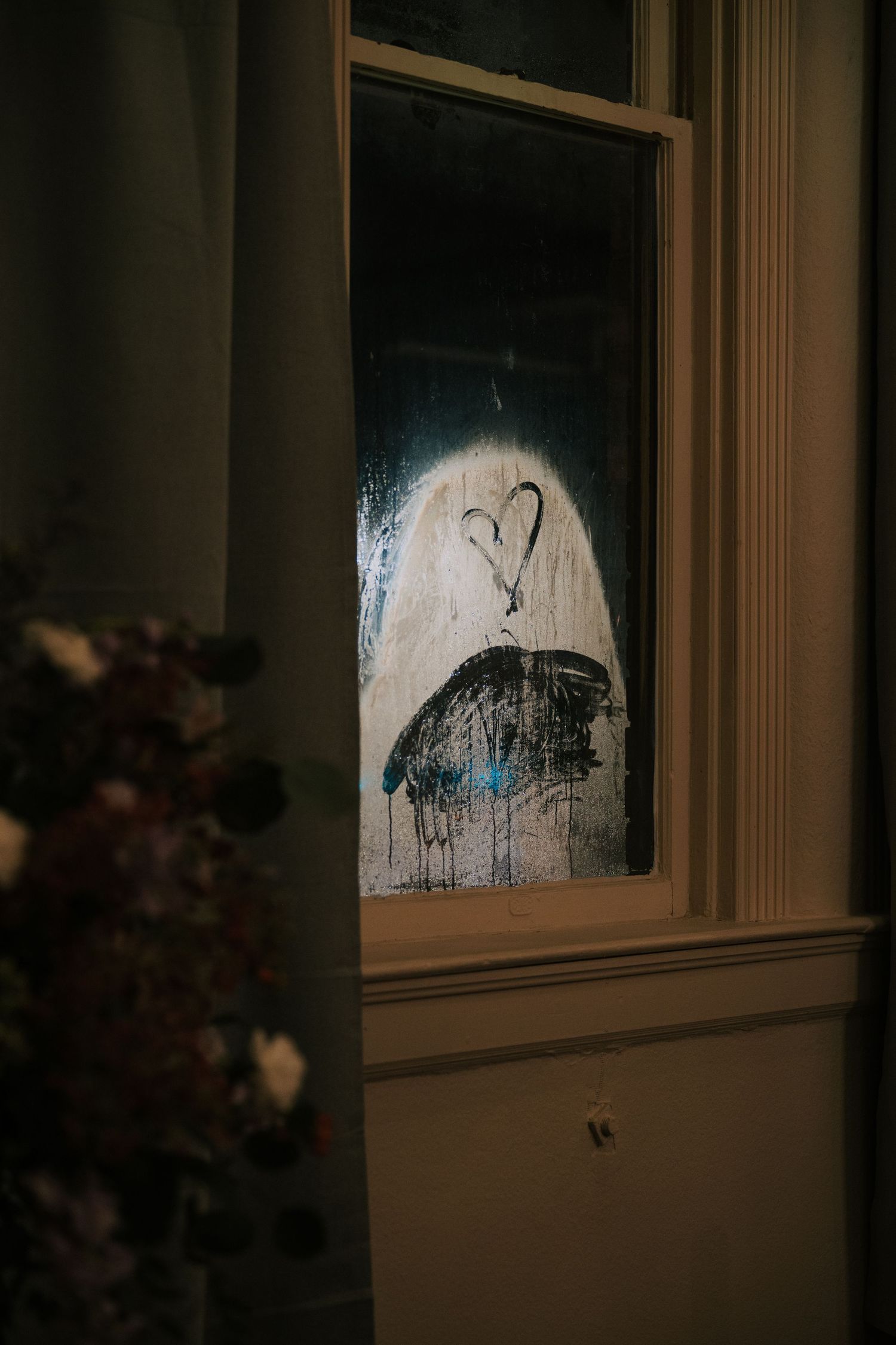 A mysterious heart and ghost-like figure drawn in condensation on a dark window pane at night.
