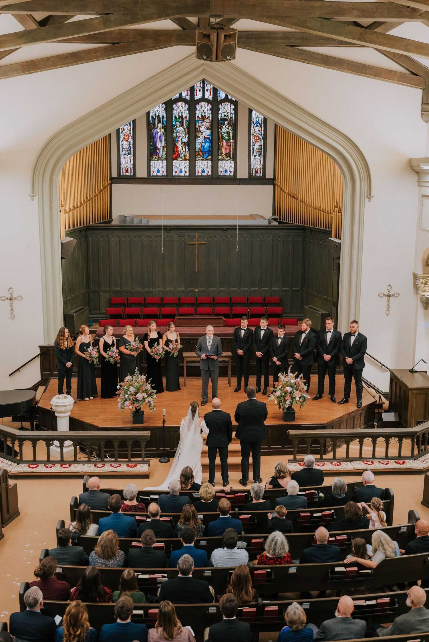 Church choir and wedding party performing during ceremony in historic chapel with stained glass windows.