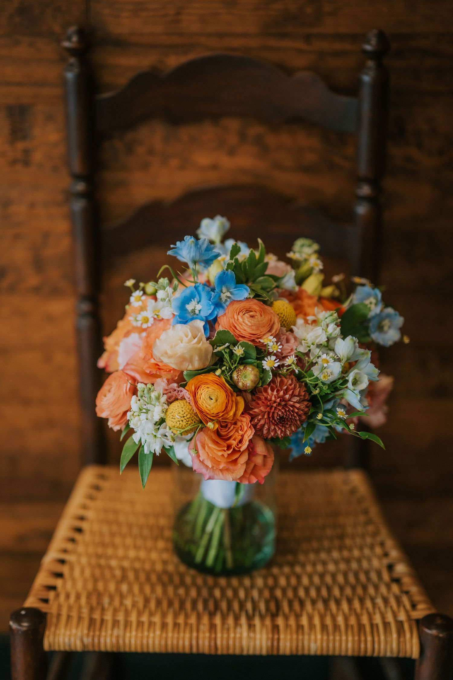 Vibrant wedding bouquet with orange, peach, and blue flowers on a rustic wooden chair.