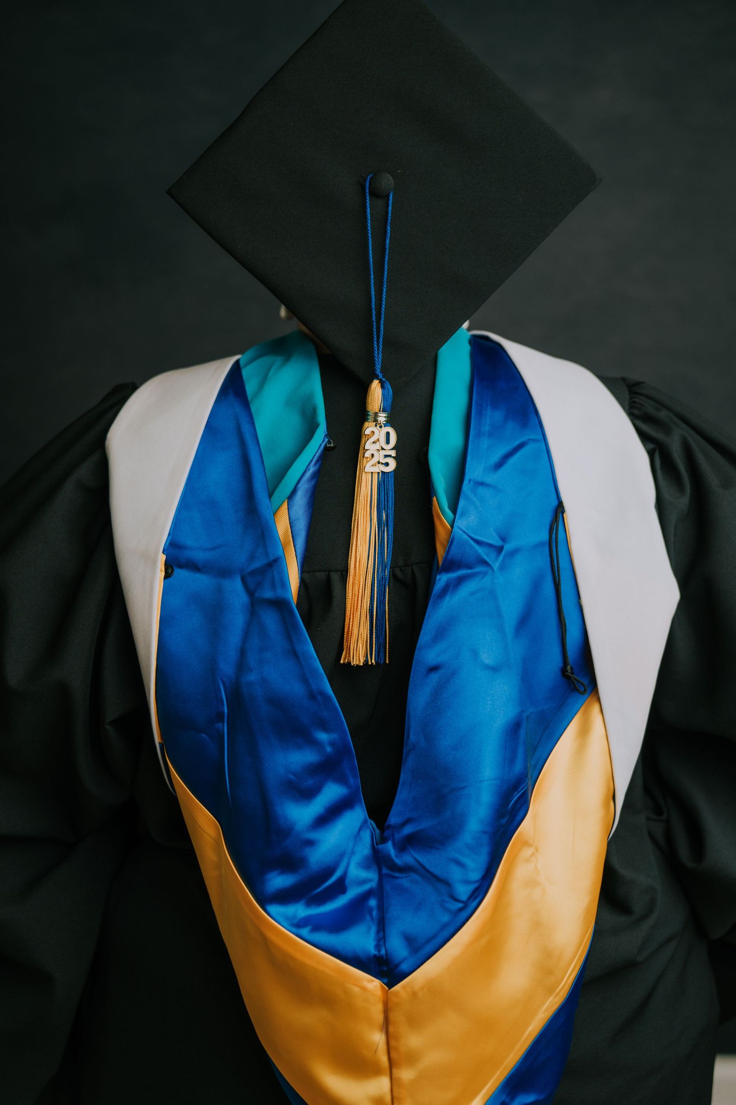 Close-up of graduation regalia showing blue and gold hood with tassel detail against dark background.