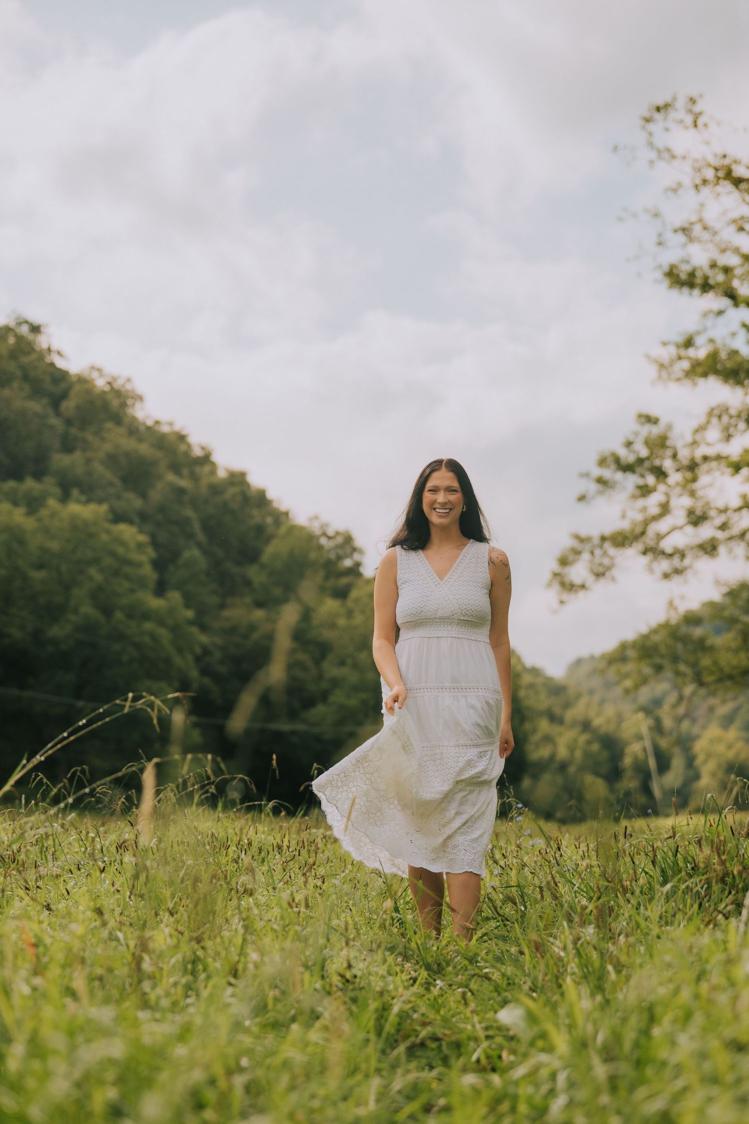 A breezy outdoor portrait in a white sundress amidst tall grass and rolling hills.