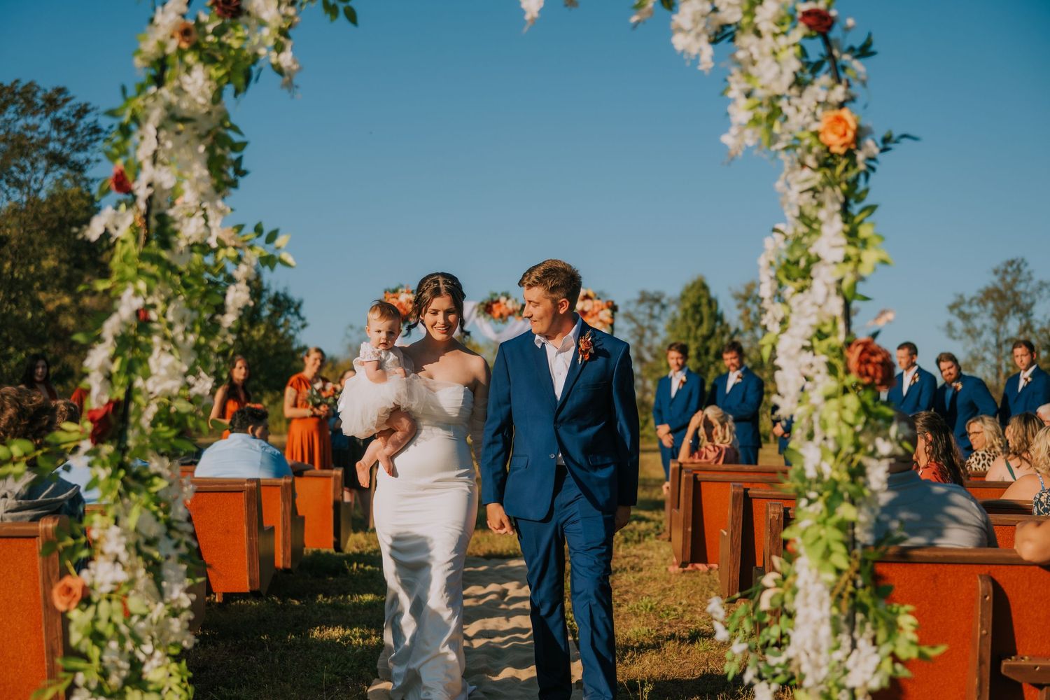 Outdoor wedding ceremony setup with floral arch against bright blue sky.