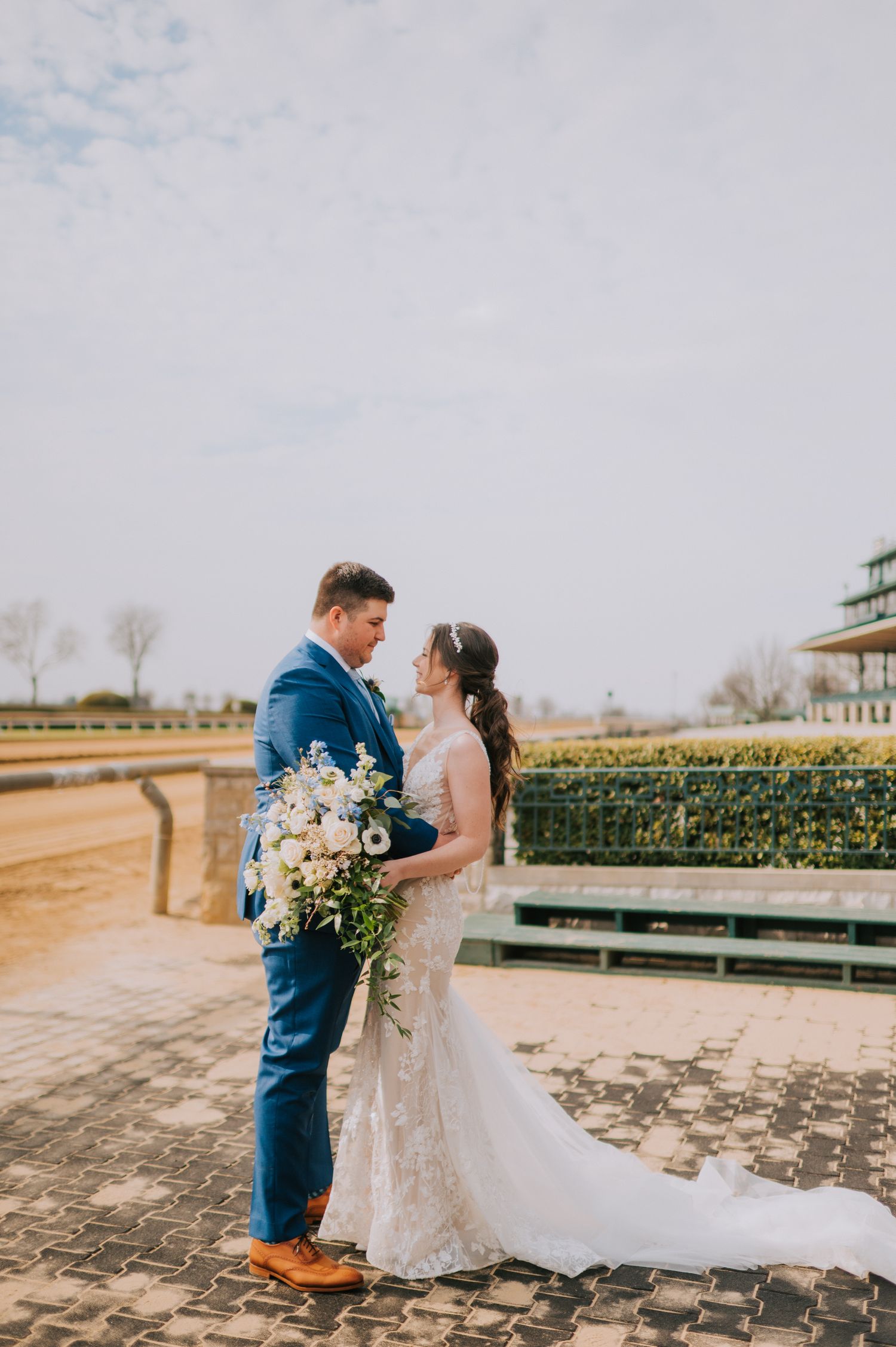 Wedding couple sharing intimate moment at racetrack venue with cloudy sky backdrop.