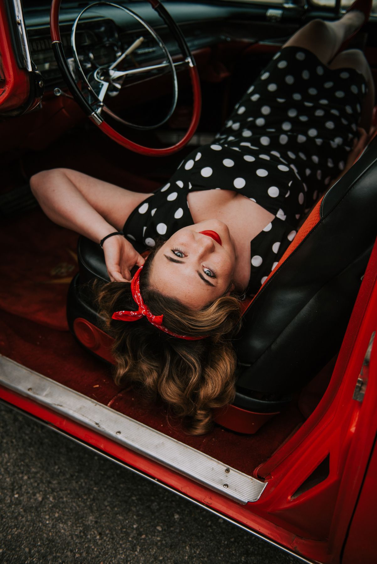 Artistic portrait series in a vintage red car featuring polka dot dress and dramatic angles.
