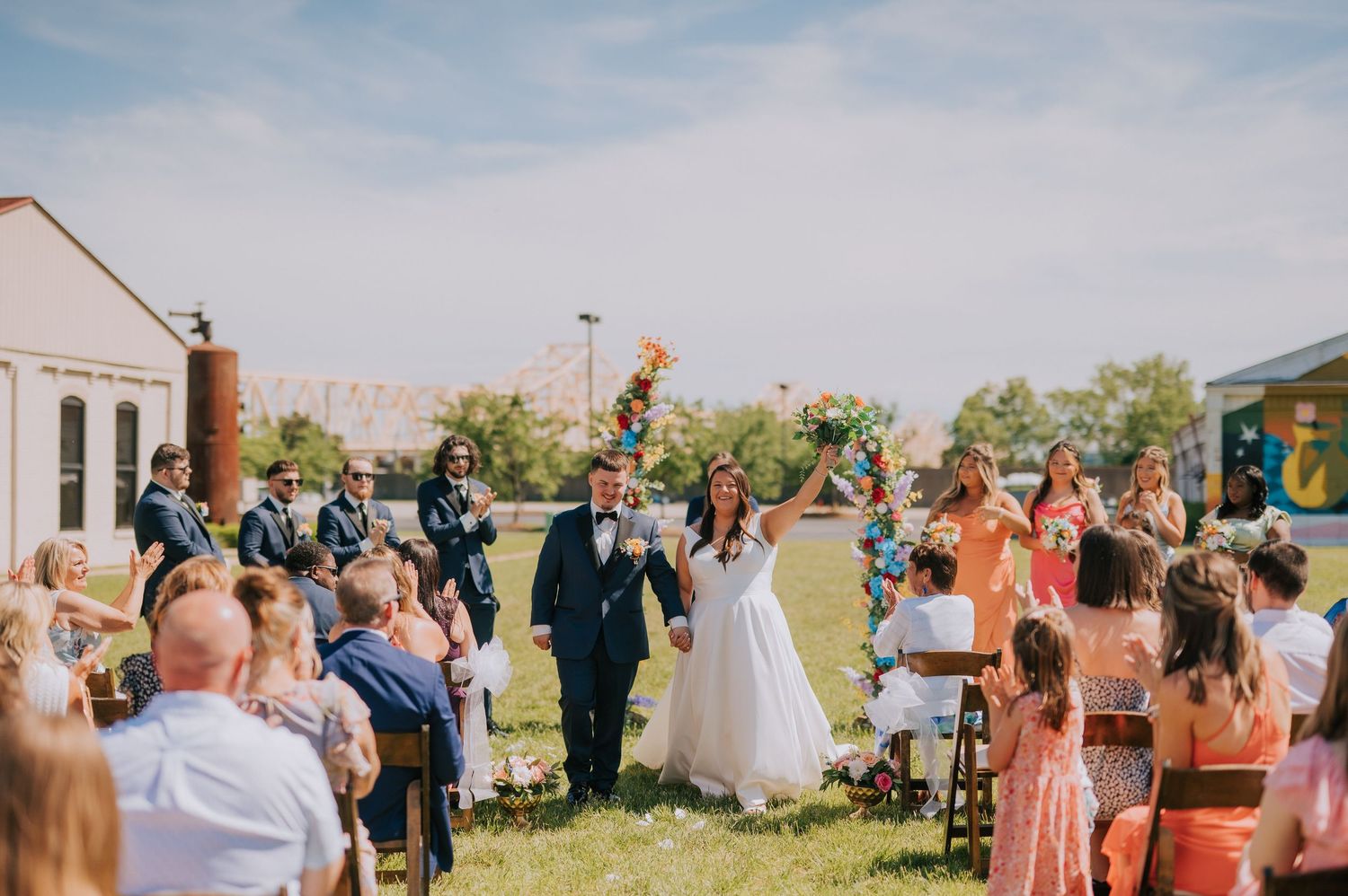 Wedding guests gather outdoors for a celebration with a church steeple visible in the background.