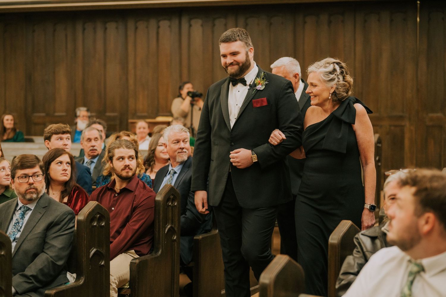Wedding guests look on as attendees walk down the aisle in a traditional church ceremony.
