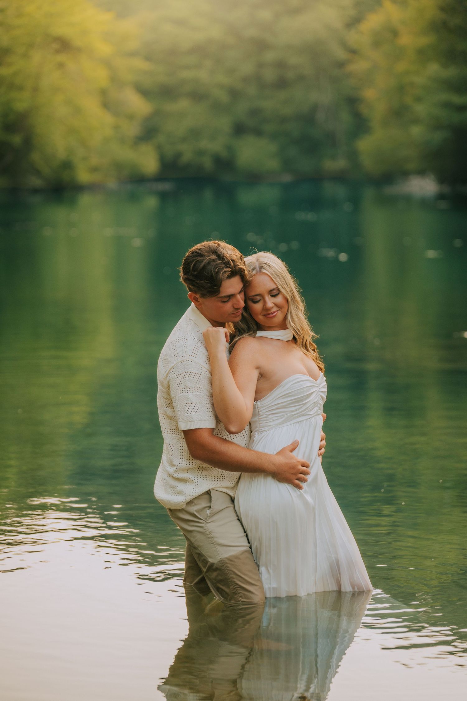 Couple embraces while standing in tranquil lake water during romantic photoshoot.