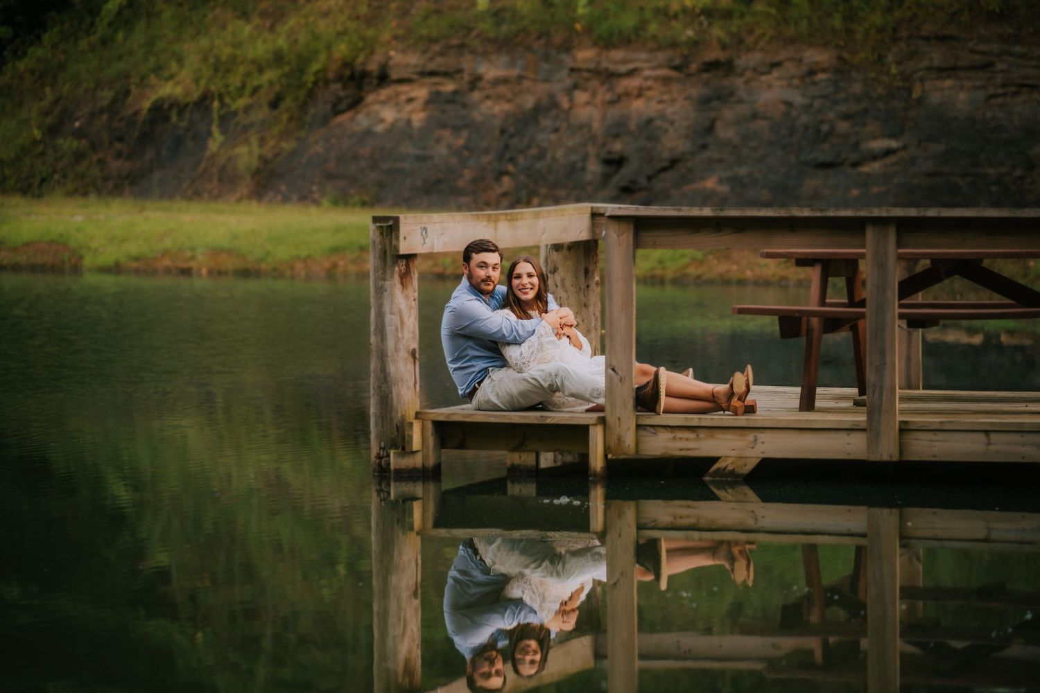 Couple shares intimate moment on wooden dock overlooking peaceful lake.
