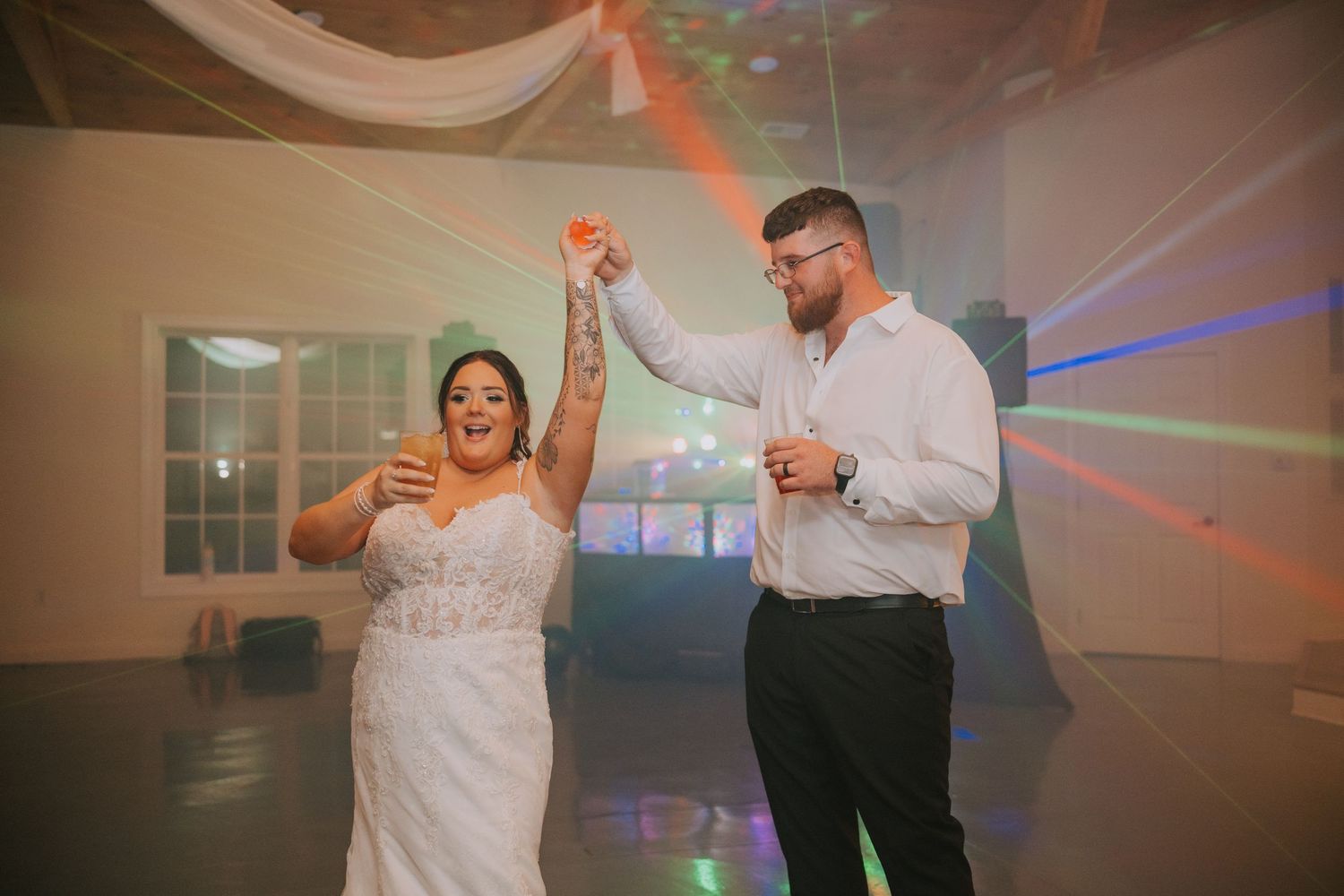 A couple dances together in a reception hall with colorful disco lights.