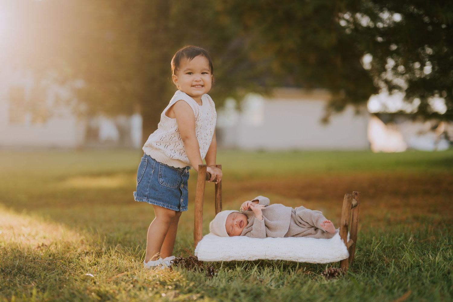 A toddler stands next to a sleeping baby outdoors during golden hour.
