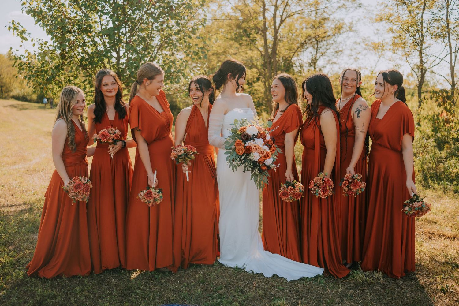 Bridesmaids in burgundy dresses pose together during fall outdoor wedding.