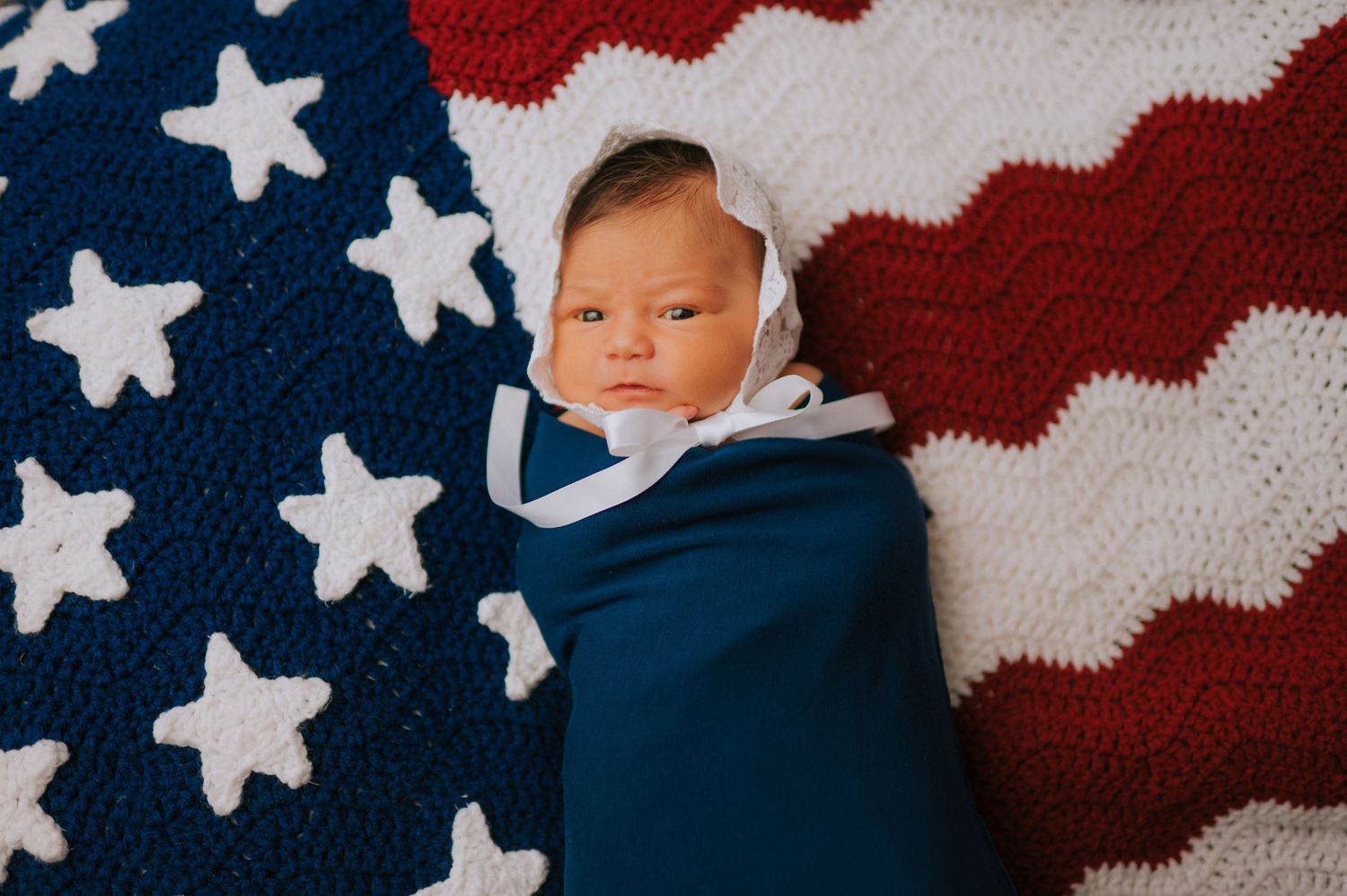 Newborn baby sleeping on patriotic American flag blanket with stars and stripes.