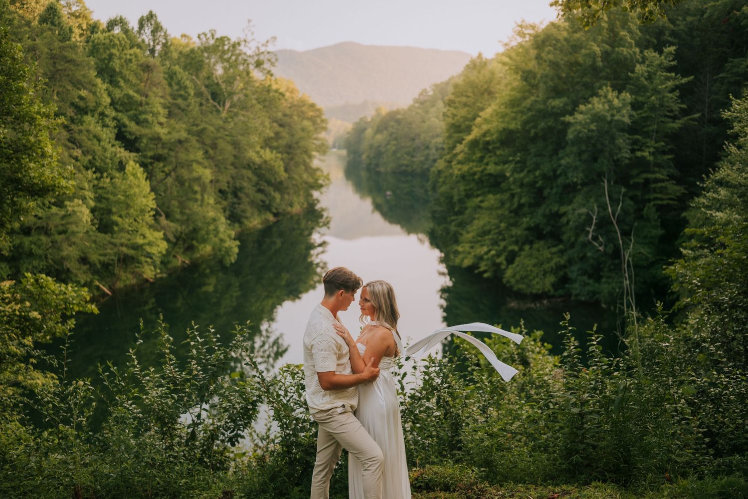 Couple sharing romantic moments by mountain lake surrounded by dense forest.