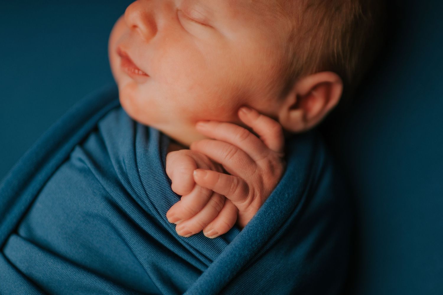 Close-up artistic newborn photography with deep blue tones and dramatic lighting.