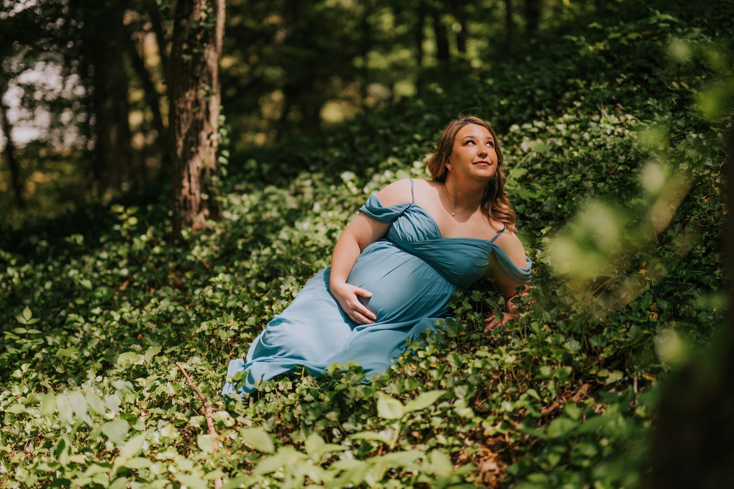 Outdoor maternity photography session with flowing teal dress in natural setting.