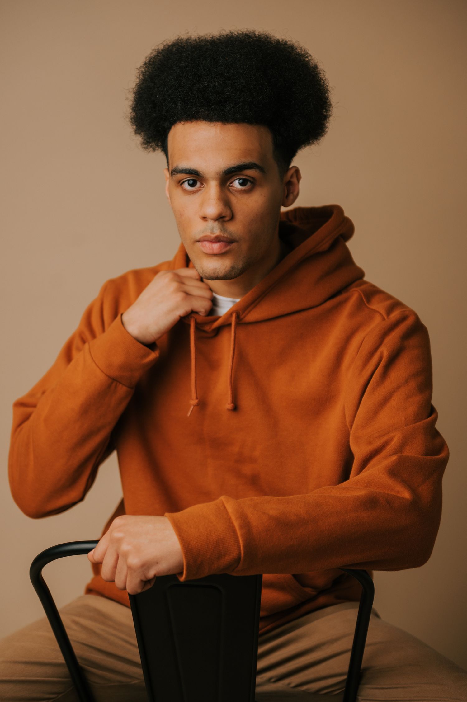 Studio portraits featuring someone in an orange hoodie seated against a warm brown background.
