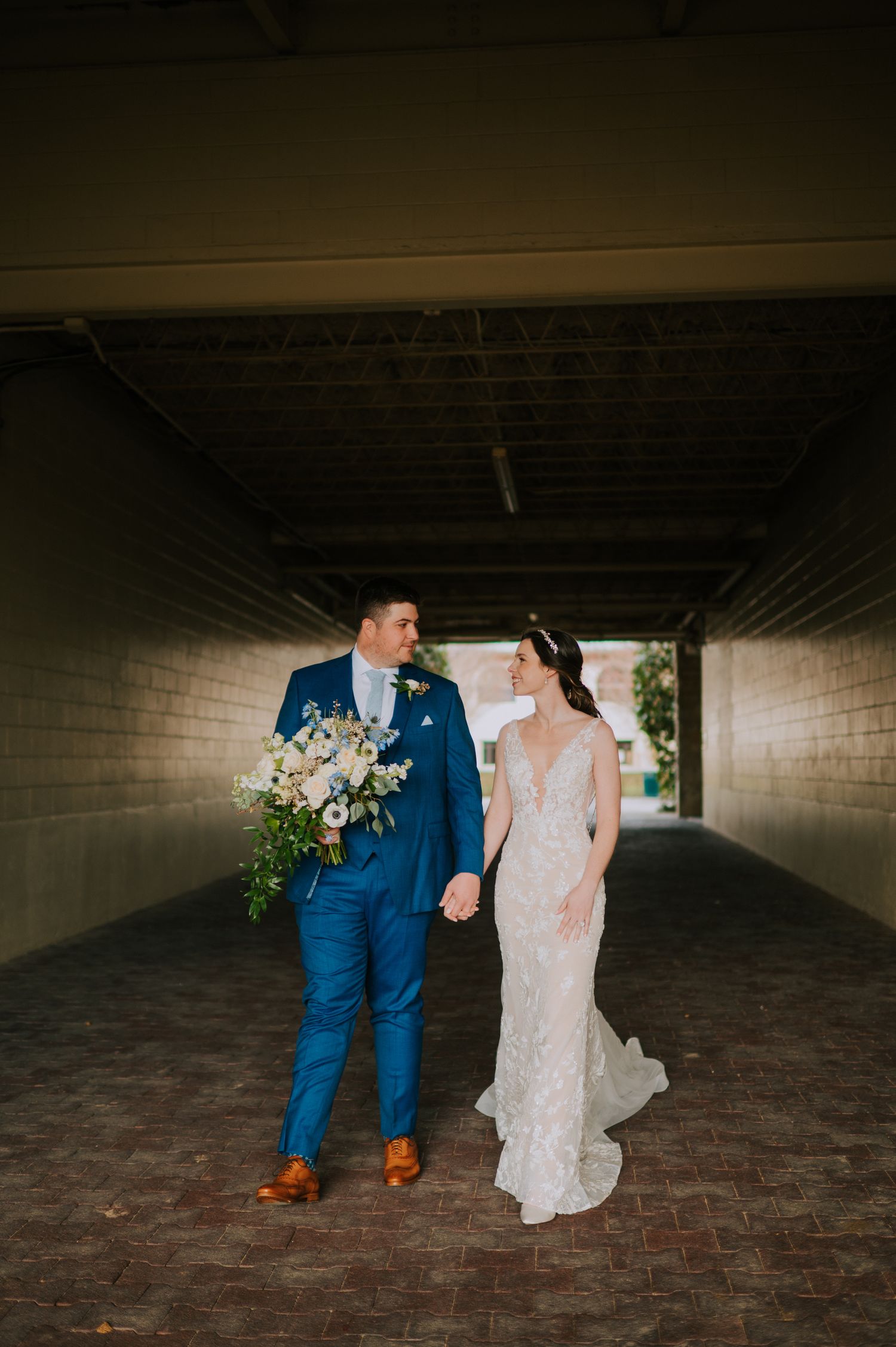Wedding couple walking through covered walkway with dramatic lighting.