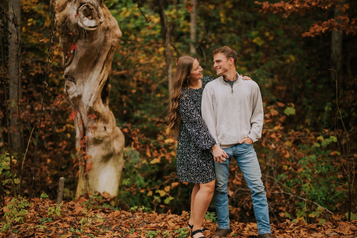 A couple shares an intimate moment while walking through fallen leaves in an autumn forest.