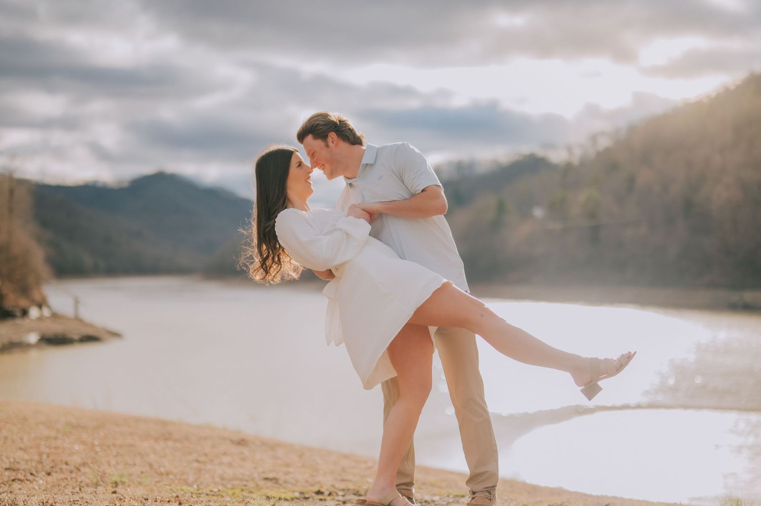 Silhouettes of a couple embracing against a dramatic mountain lake backdrop at sunset.