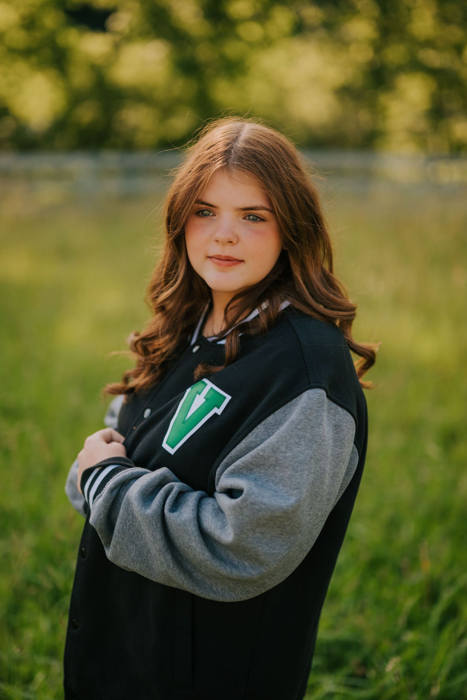 Student wearing varsity letterman jacket poses in outdoor field setting.
