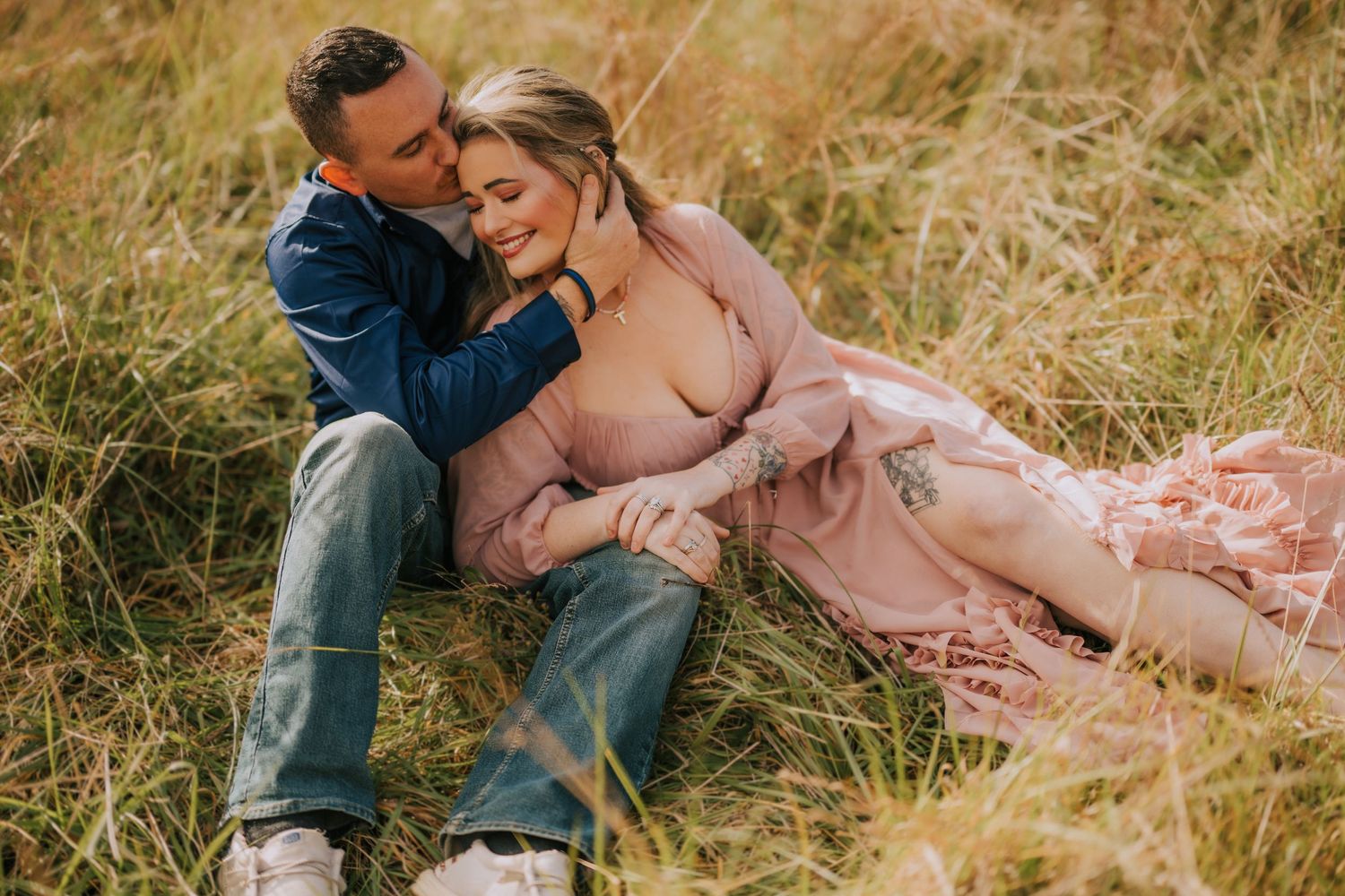 Intimate couple poses together in tall grass during golden hour photoshoot.