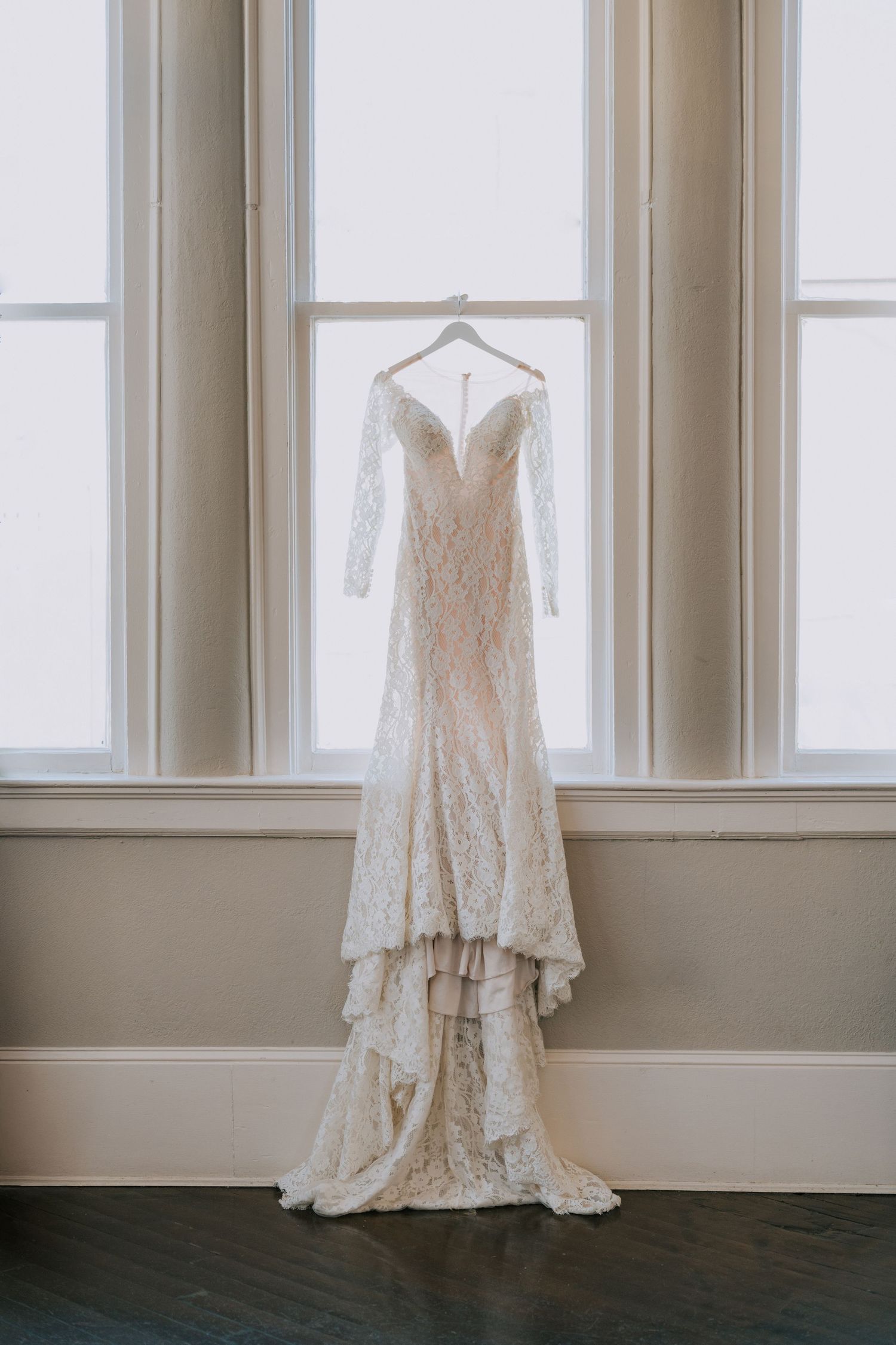 Elegant lace wedding dress with long sleeves hanging in bright window display.