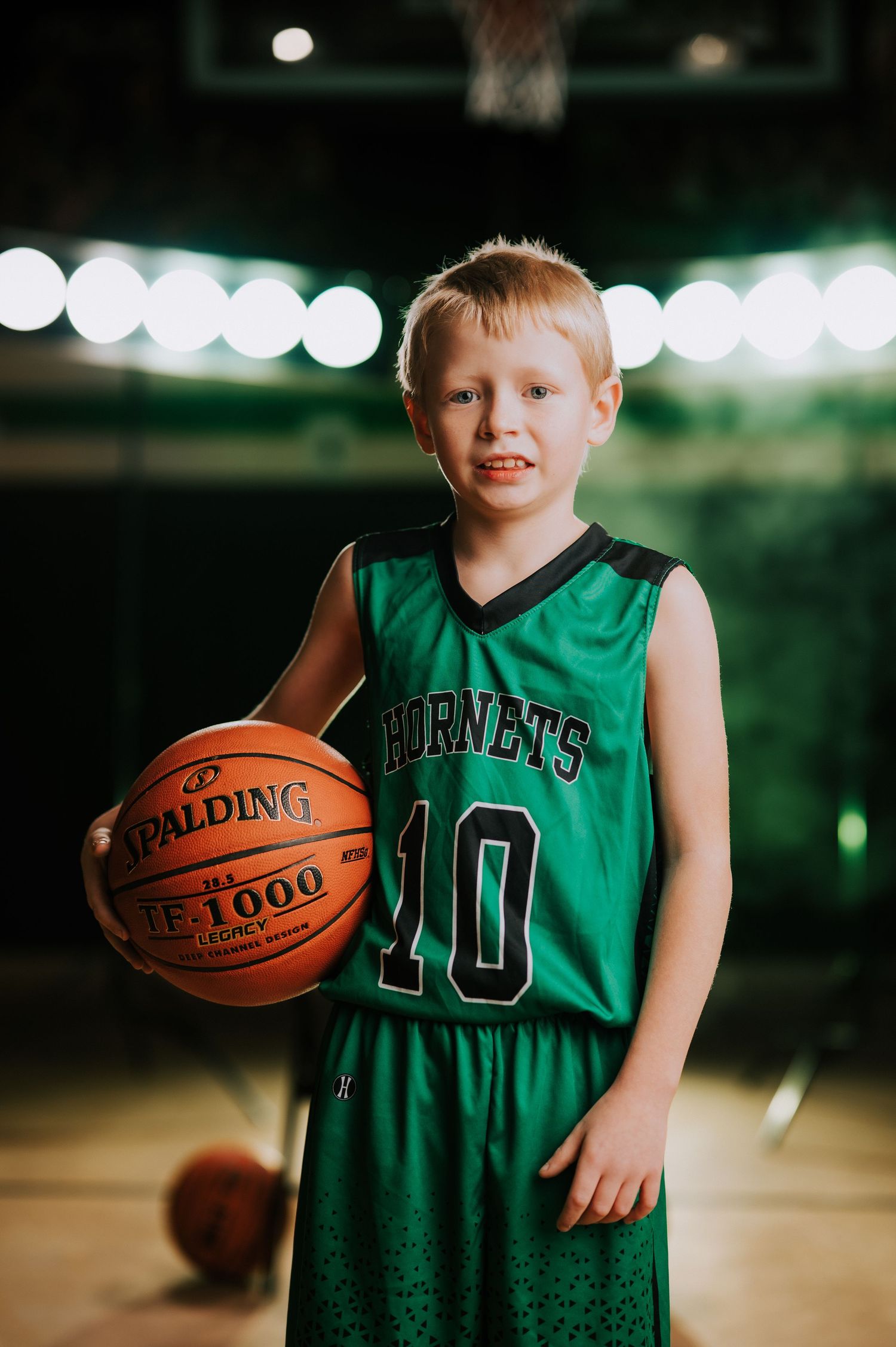 Youth basketball player in green Hornets jersey poses with ball in gymnasium.