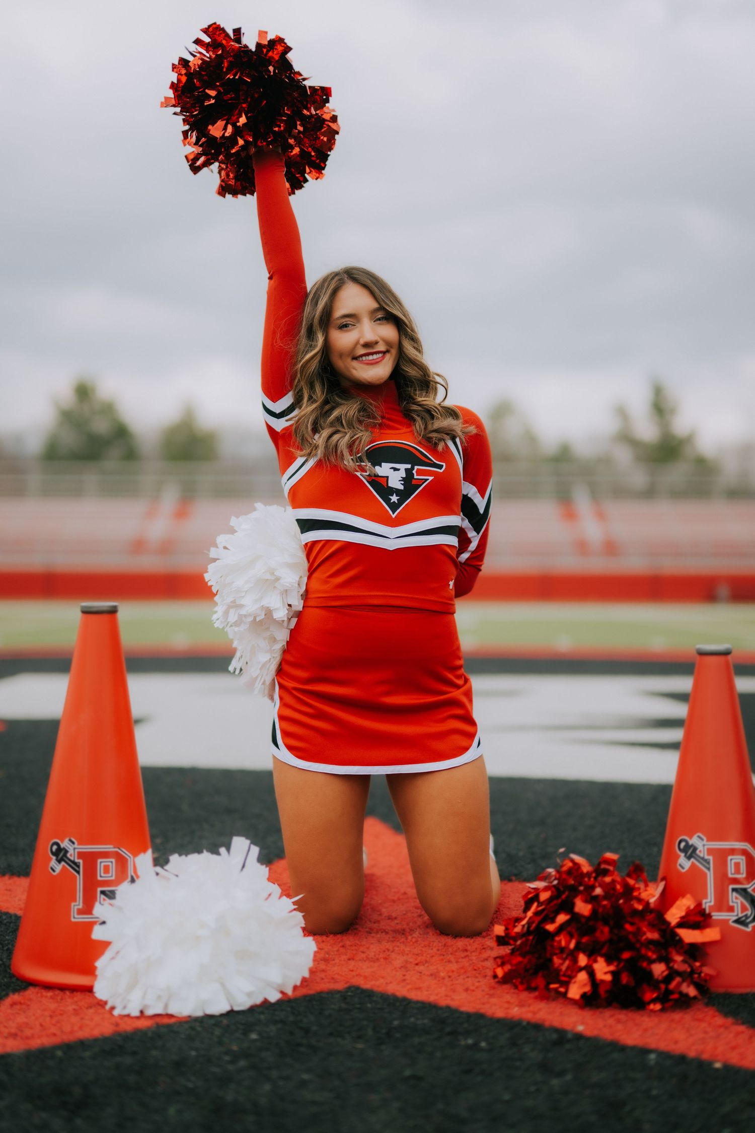 A cheerleader in red uniform poses with pom poms on a field with orange traffic cones in a creative photo series.