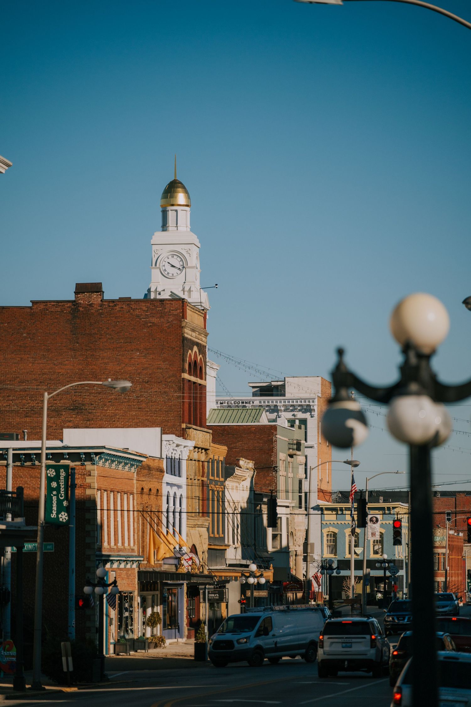 Historic downtown street with brick buildings and a prominent white clock tower against a bright blue sky.