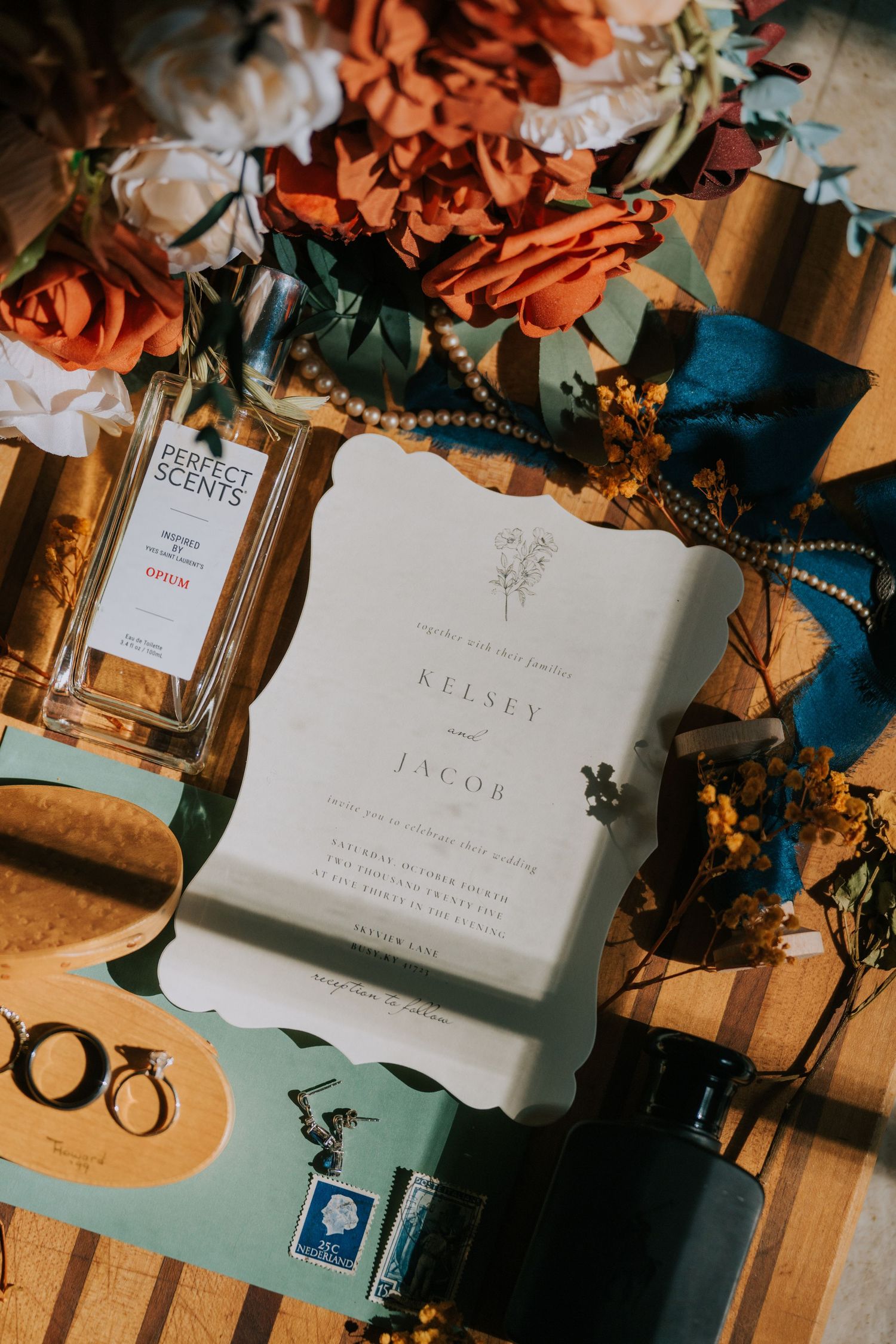 Wedding invitation cards with orange floral decorations and blue accents arranged on a wooden surface in warm lighting.