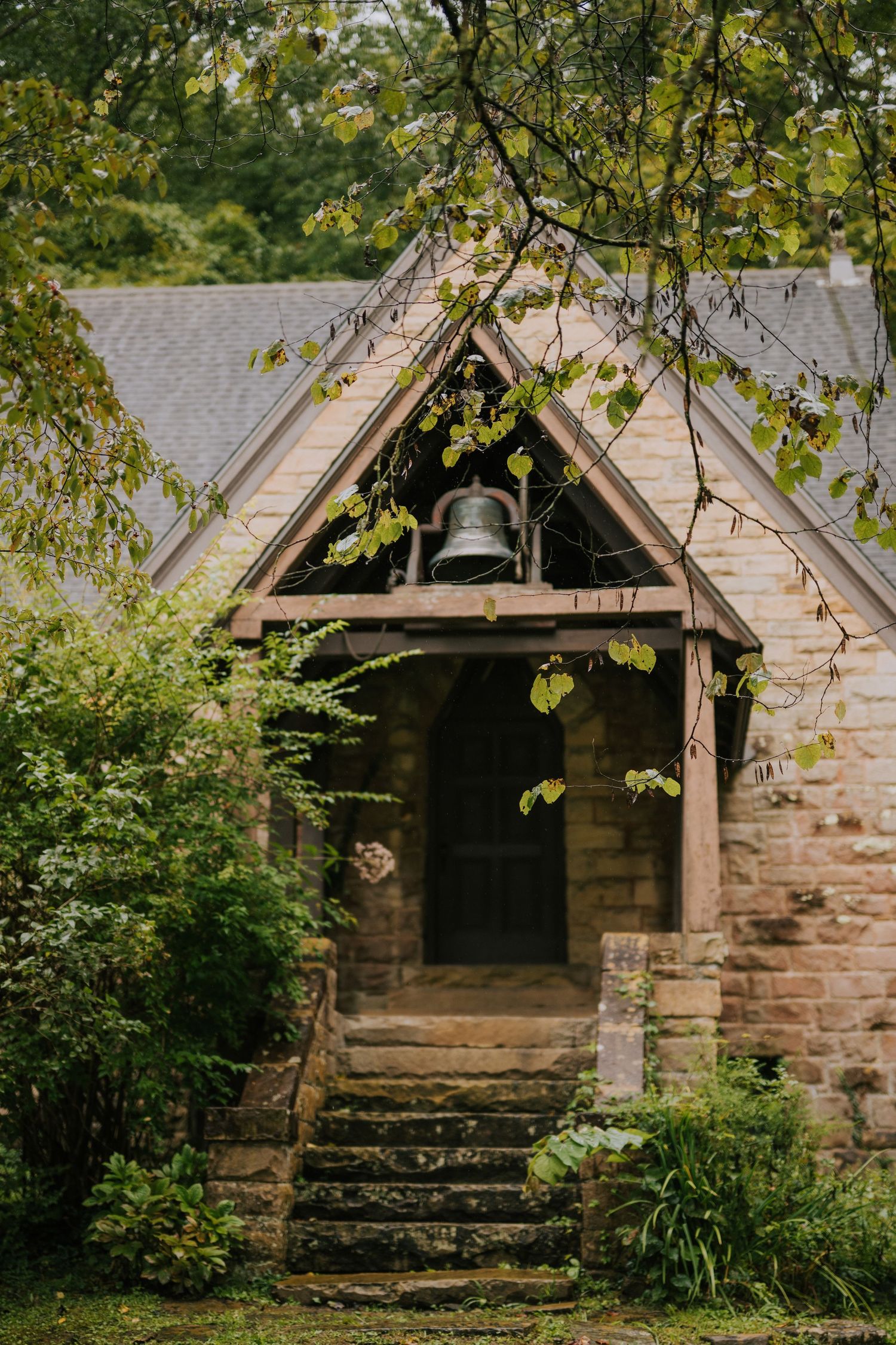 A rustic stone chapel or small building nestled among green trees and foliage.