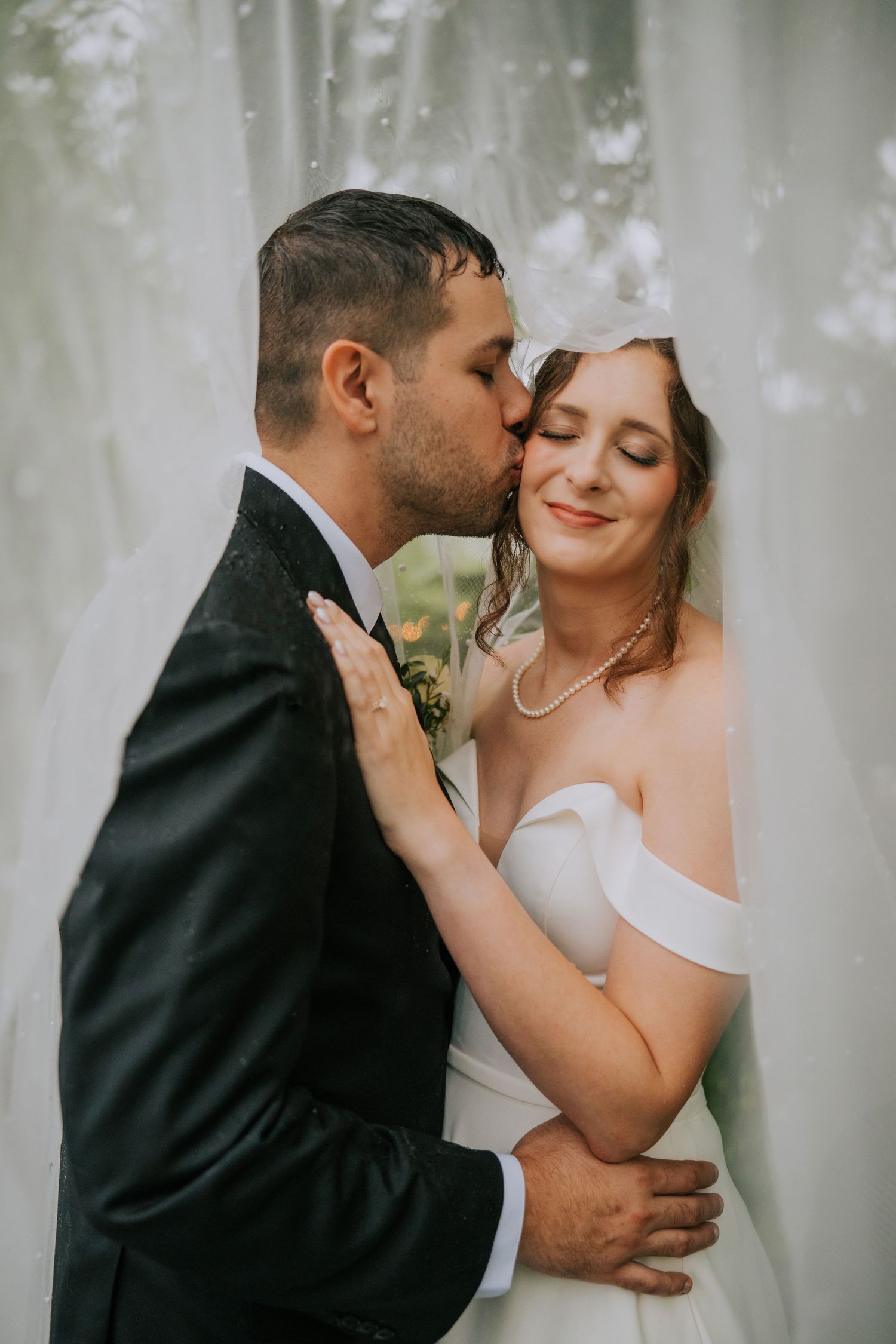 Intimate moment between newlyweds captured through flowing white veil during wedding portraits.