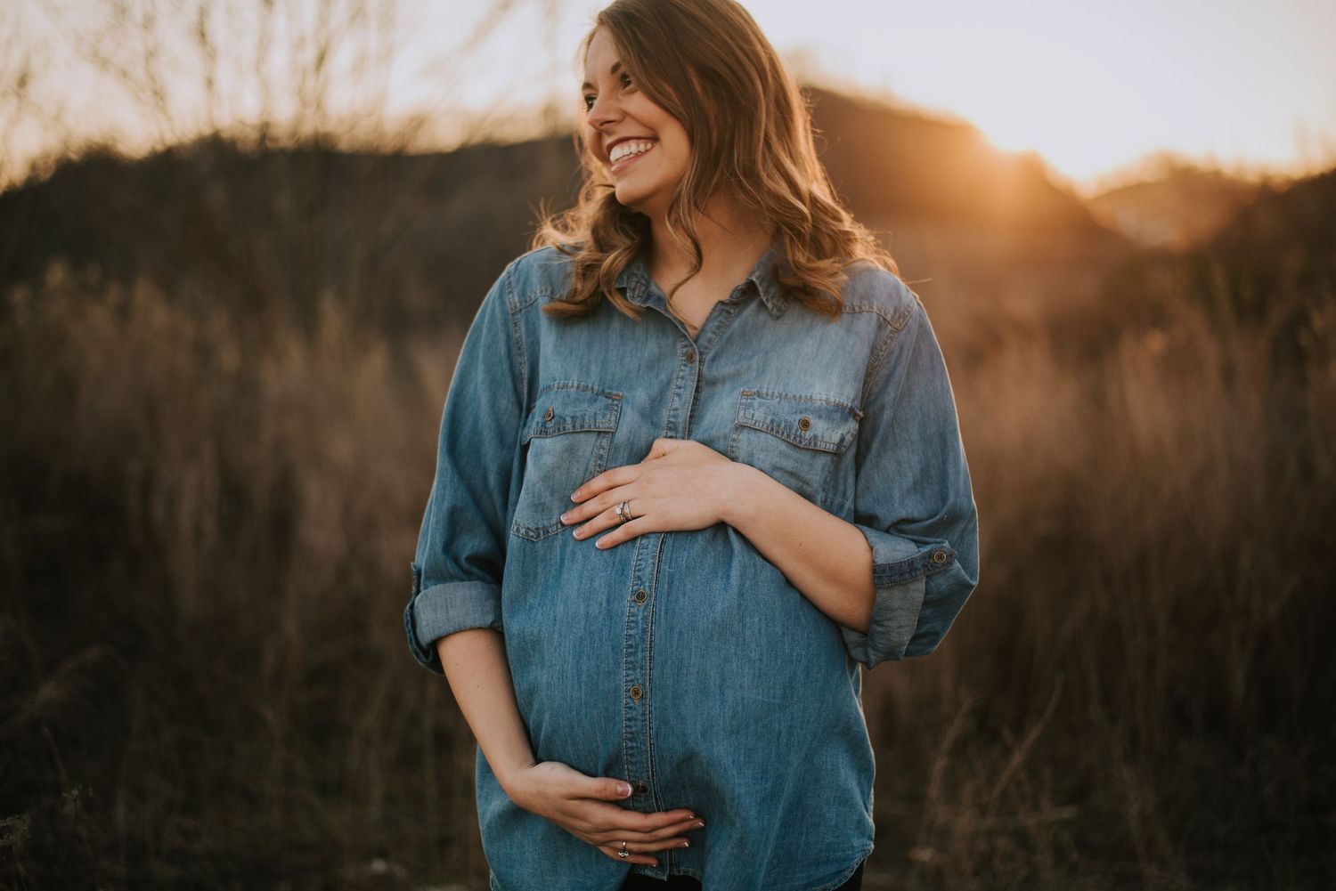 Sunset maternity session featuring denim shirt in golden field.