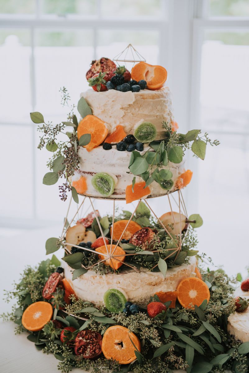 Three-tiered white wedding cake decorated with orange slices, greenery and berries.