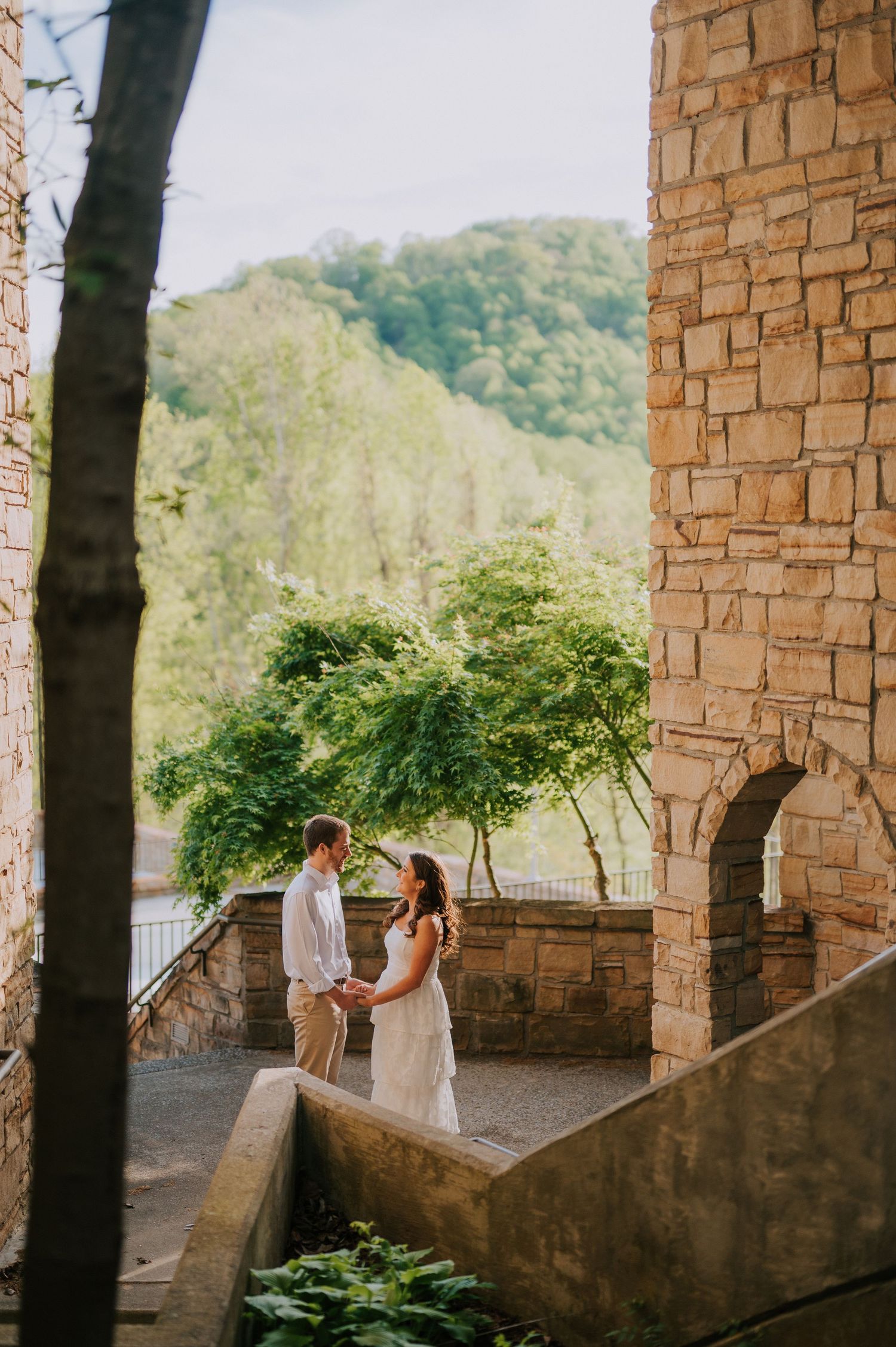 A couple shares a moment under stone archways overlooking a scenic mountain landscape.