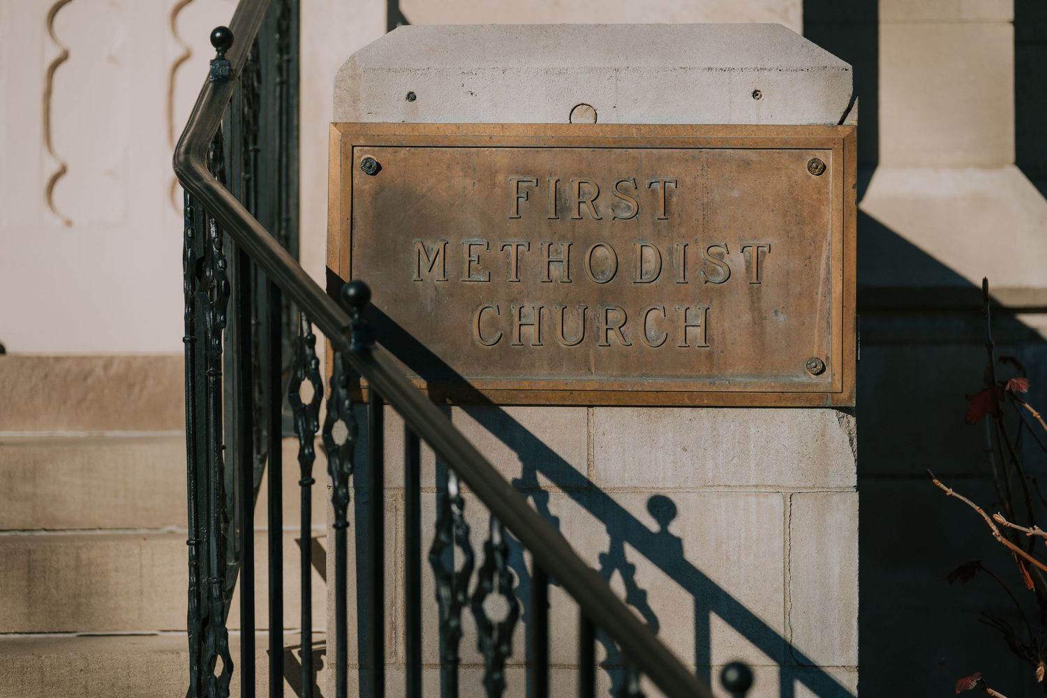 A vintage brass plaque reading 'First Methodist Church' mounted on a stone wall beside decorative iron railings.
