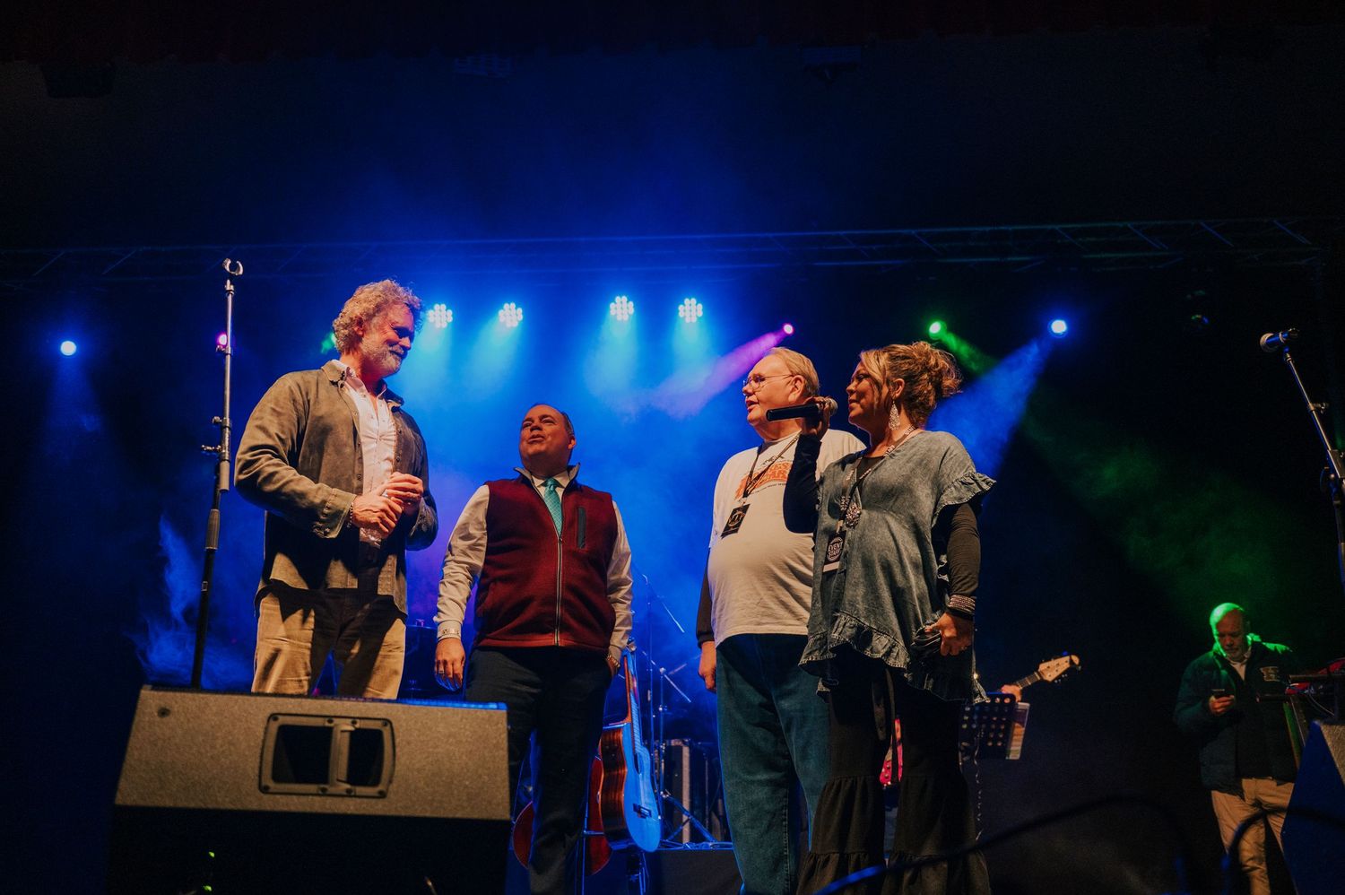 Musicians perform together on a stage with blue lighting and professional sound equipment.