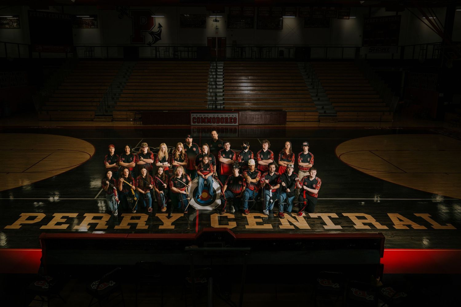 A basketball team poses for a group photo on their home court with Perry Central branding visible on the floor.