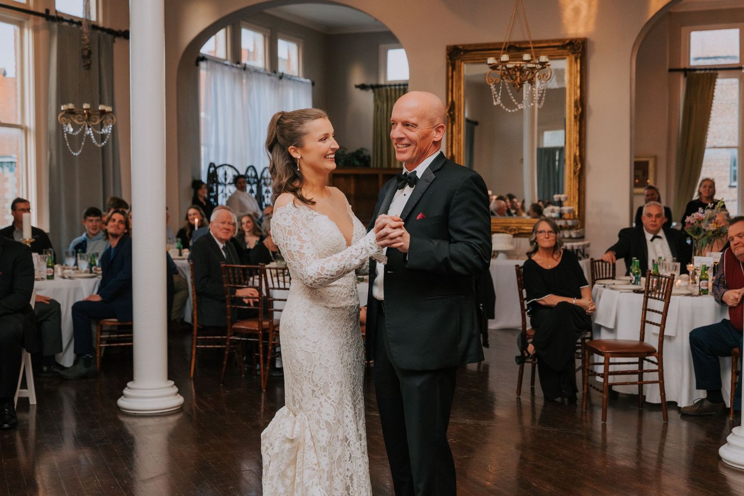 A tender moment during a first dance at an elegant wedding reception in a classic ballroom with white columns.