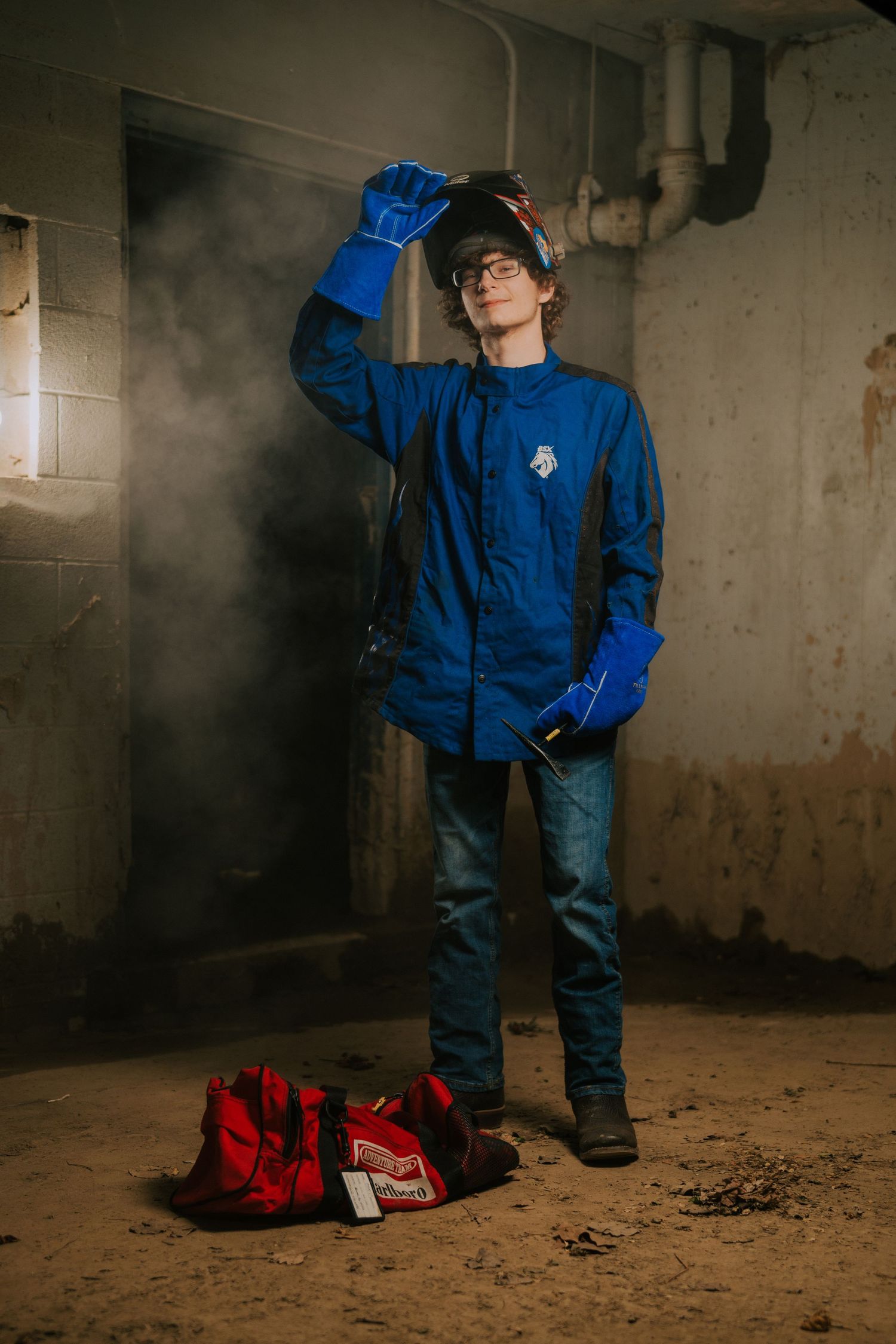 Person in blue workwear poses dramatically in industrial basement setting.